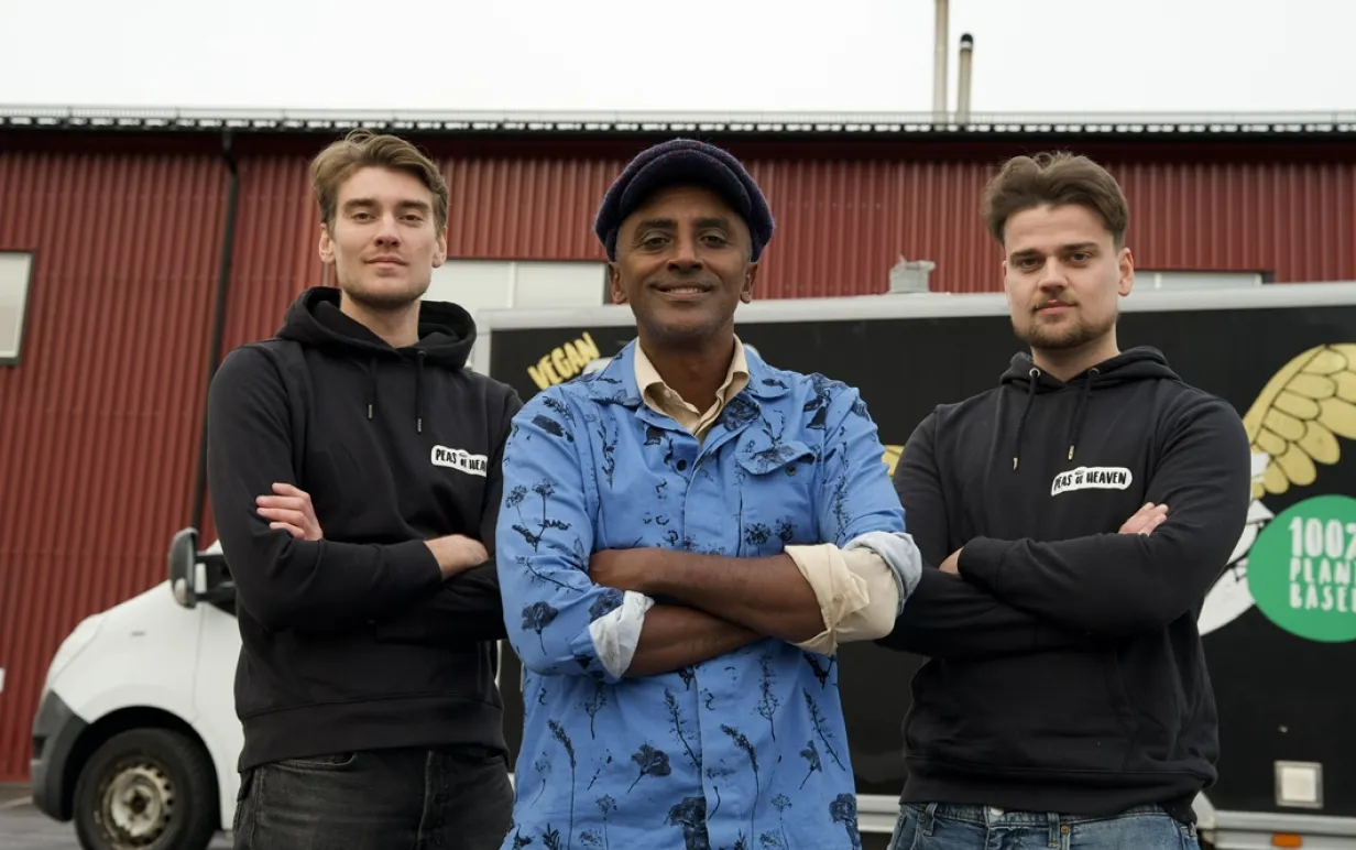 Tre män som står uppradade mot en röd vägg