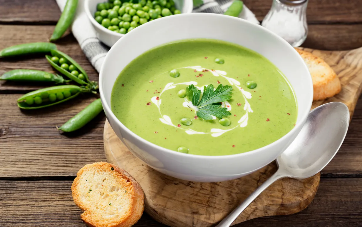en skål med grön ärtsoppa på en underlägg i trä