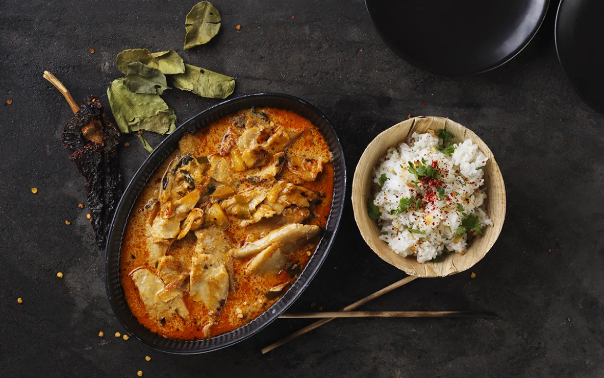 Vegansk röd curry i en gryta bredvid en skål ris på ett svart bord