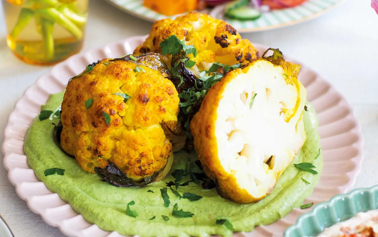 Rostad blomkål med grön tahinisås på en vit tallrik