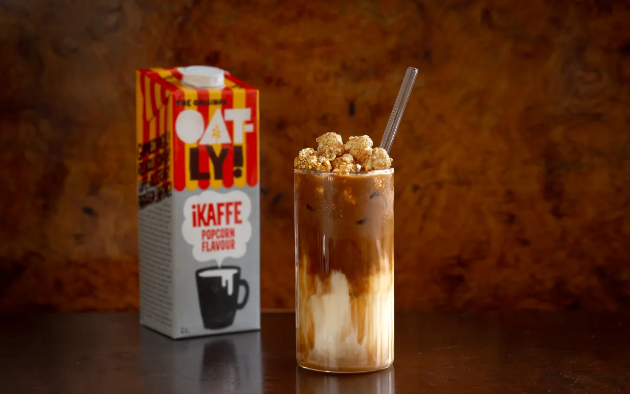 En förpackning havredryck bakom ett glas med en iskaffe på ett bord