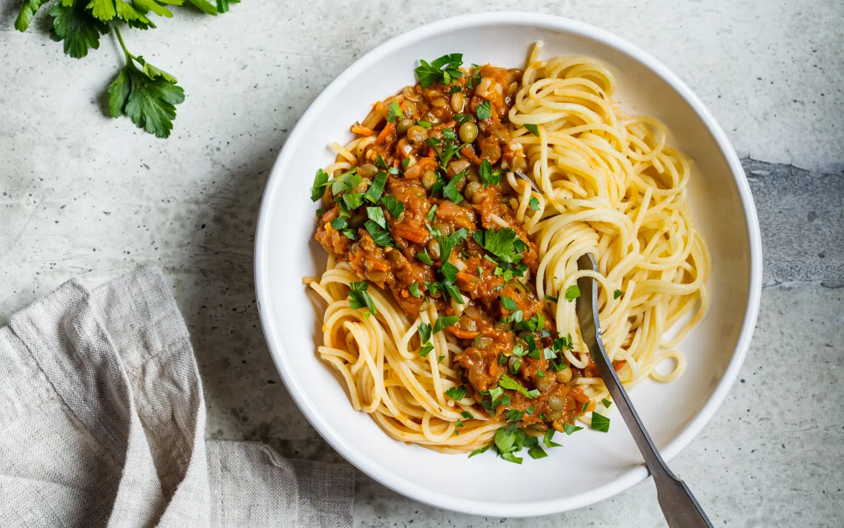 Vegansk bolognese på linser med spaghetti i en vit tallrik på ett bord