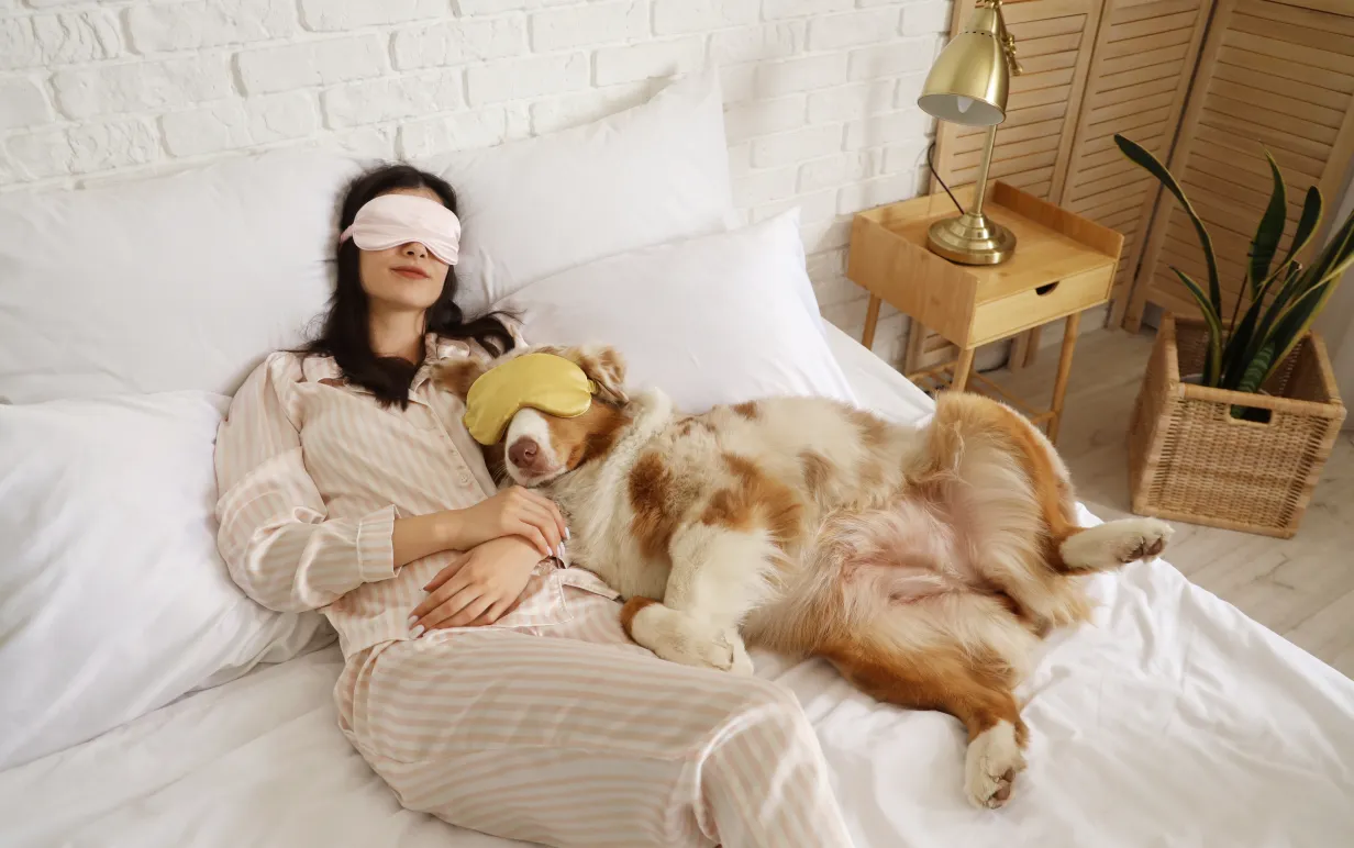 Kvinna som sover med sin hund och båda använder ögonmask