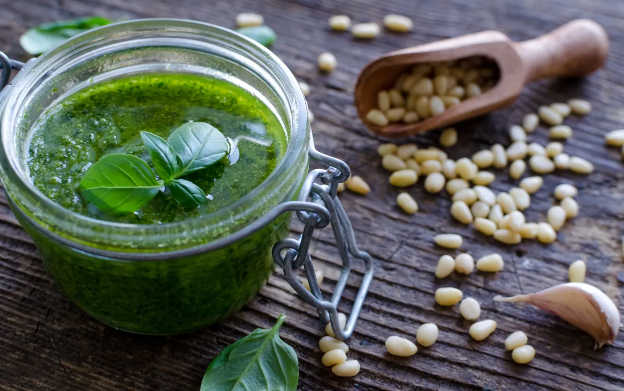 Bild på grönpesto på ett bord med utrströdda pinjenötter.