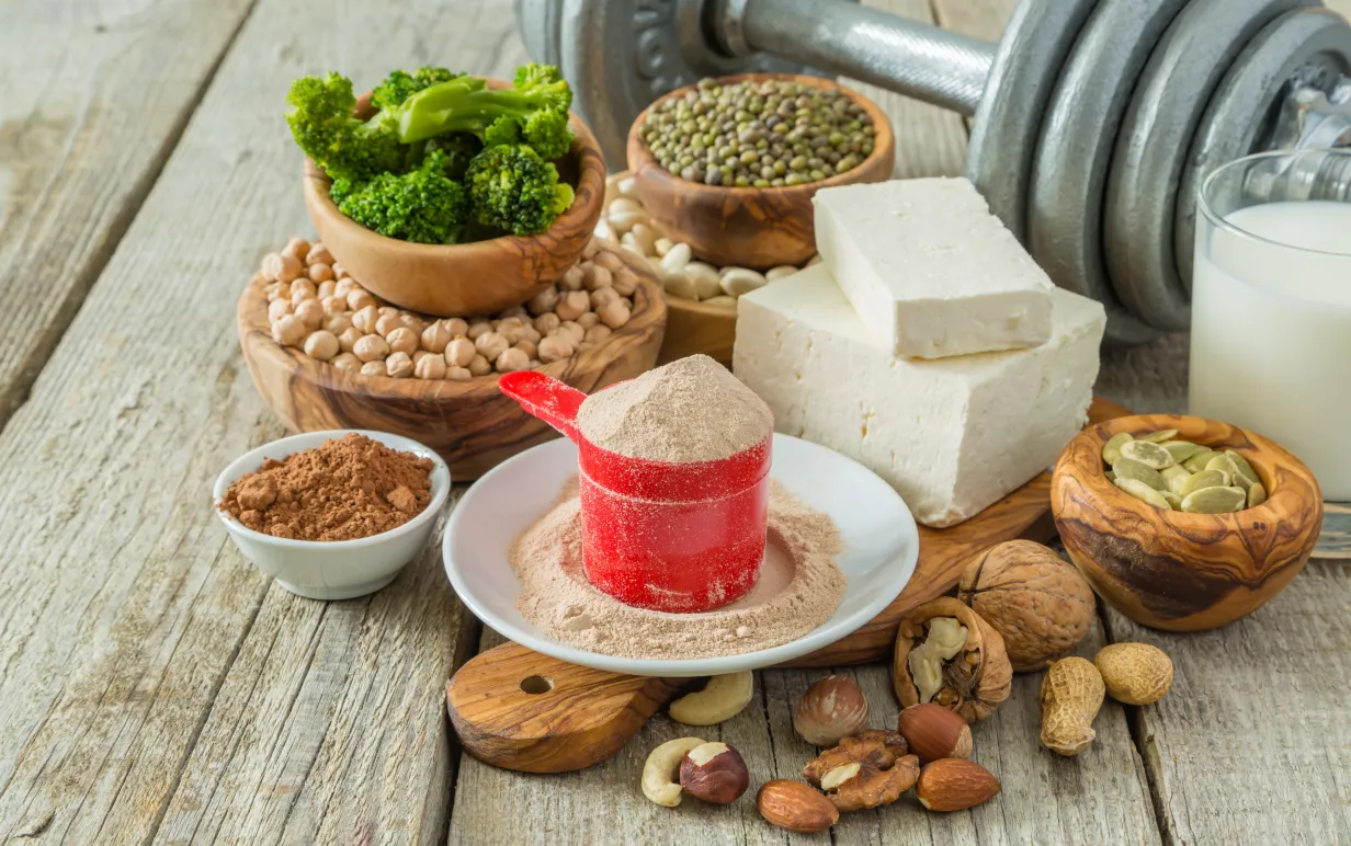 Bild på olika vegetabilsika proteinkällor och en träningsvikt i bakgrunden