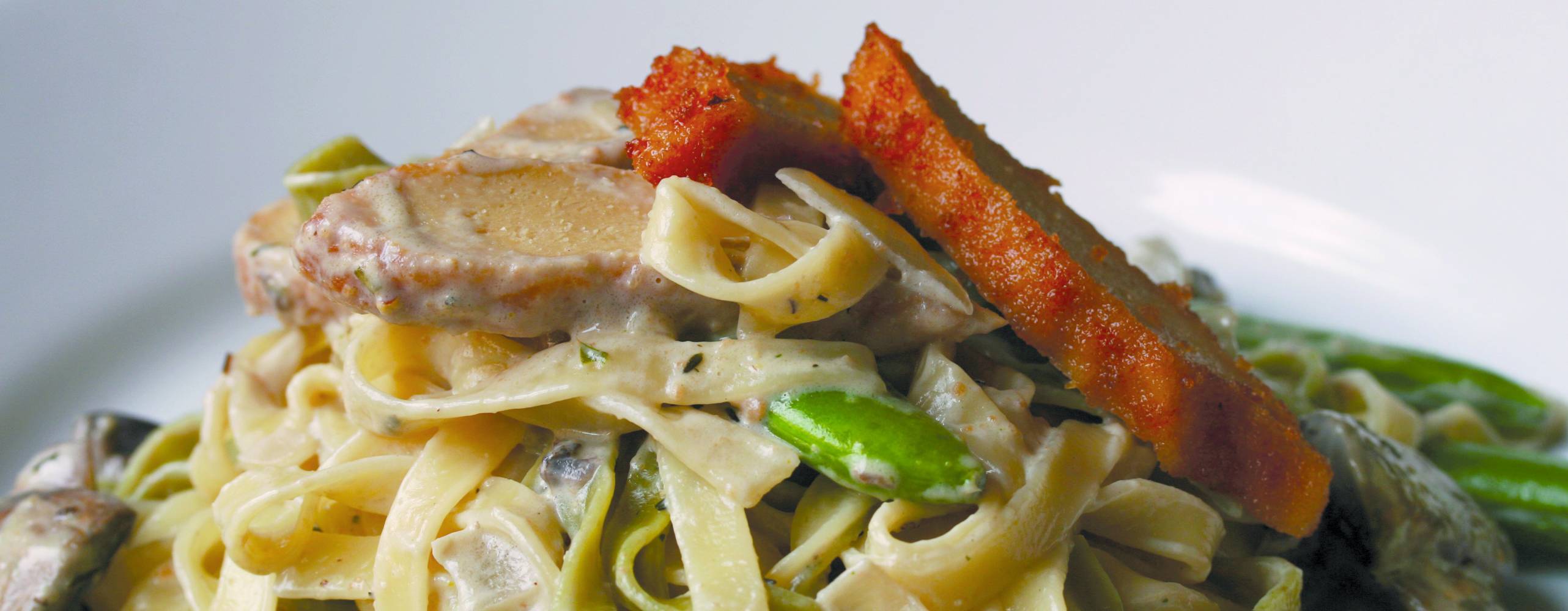 Pasta med sojakyckling och sockerärtor på en vit tallrik