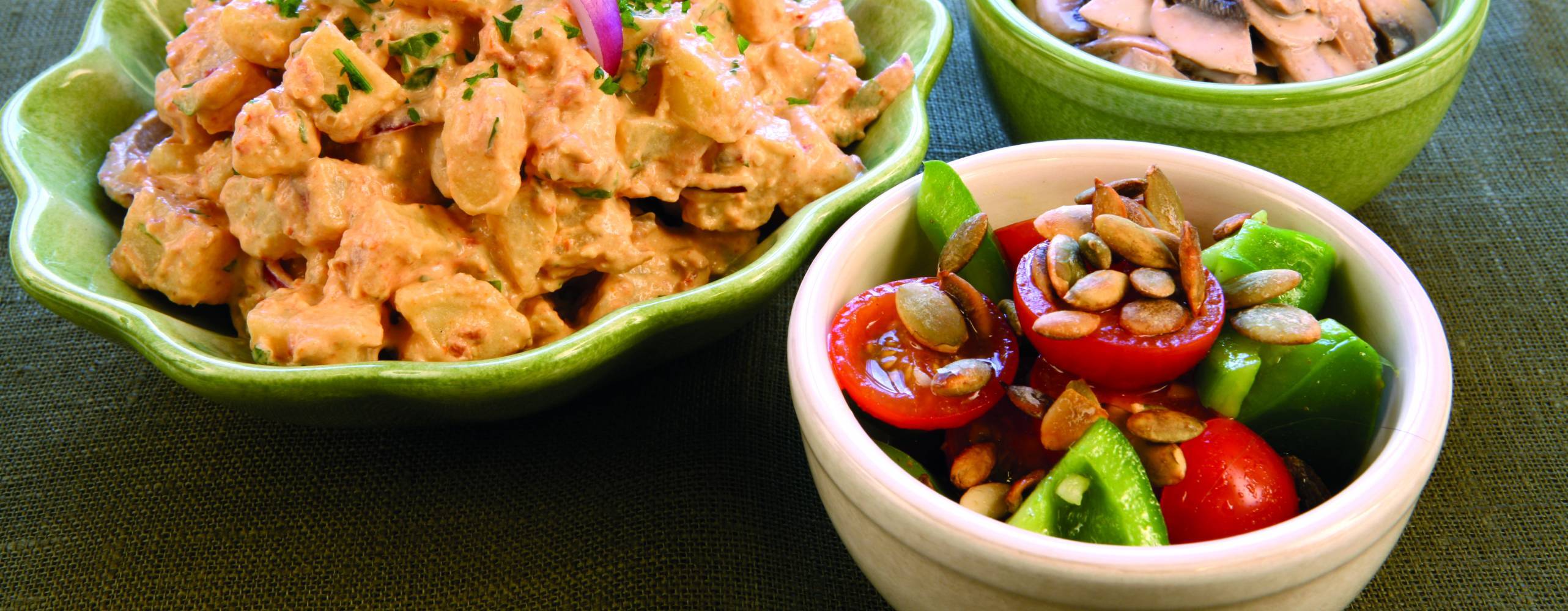 Tre skålar, en med potatissallad, en med råa champinjoner och en med tomat och paprika.