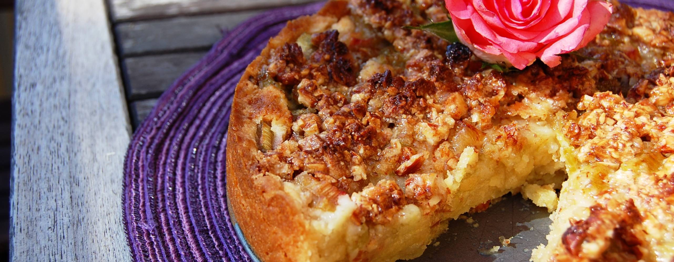 Rabarbertårta dekorerad med en rosa ros, på en lila duk.