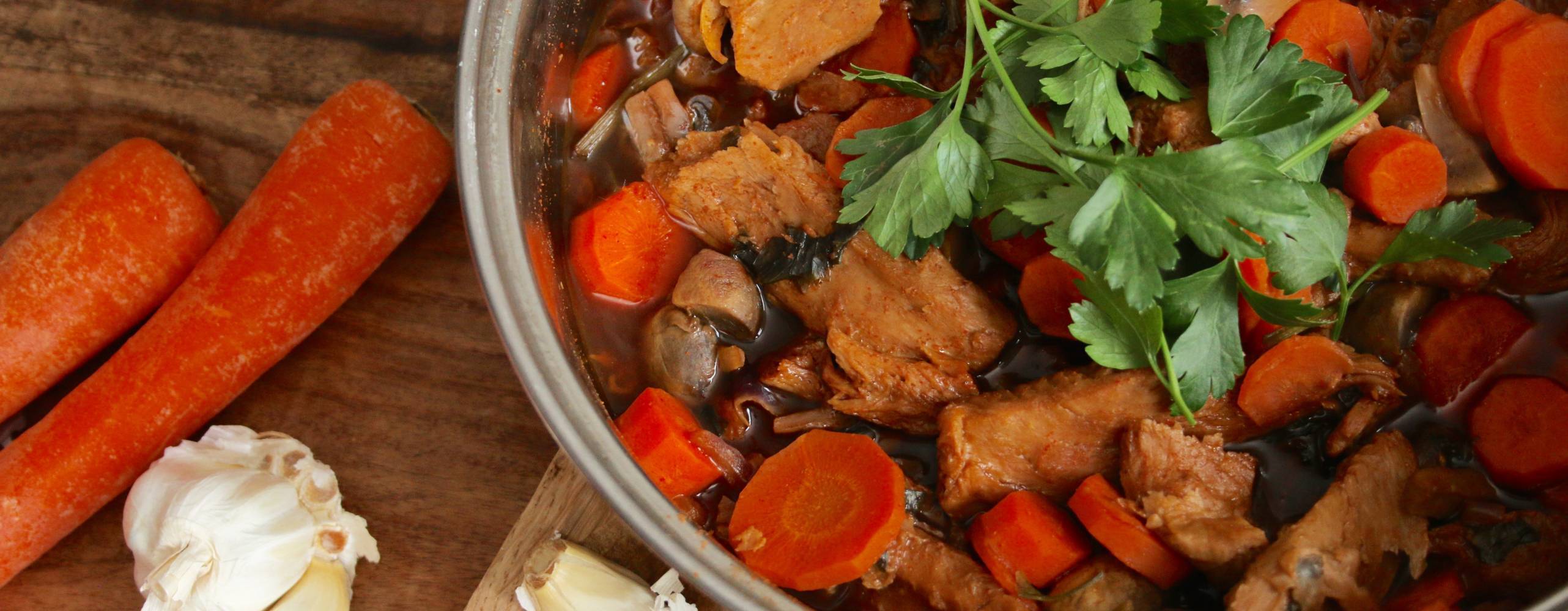 en tallrik med mustig viltgryta på ett bord, bredvid ligger några morötter och en vitlök