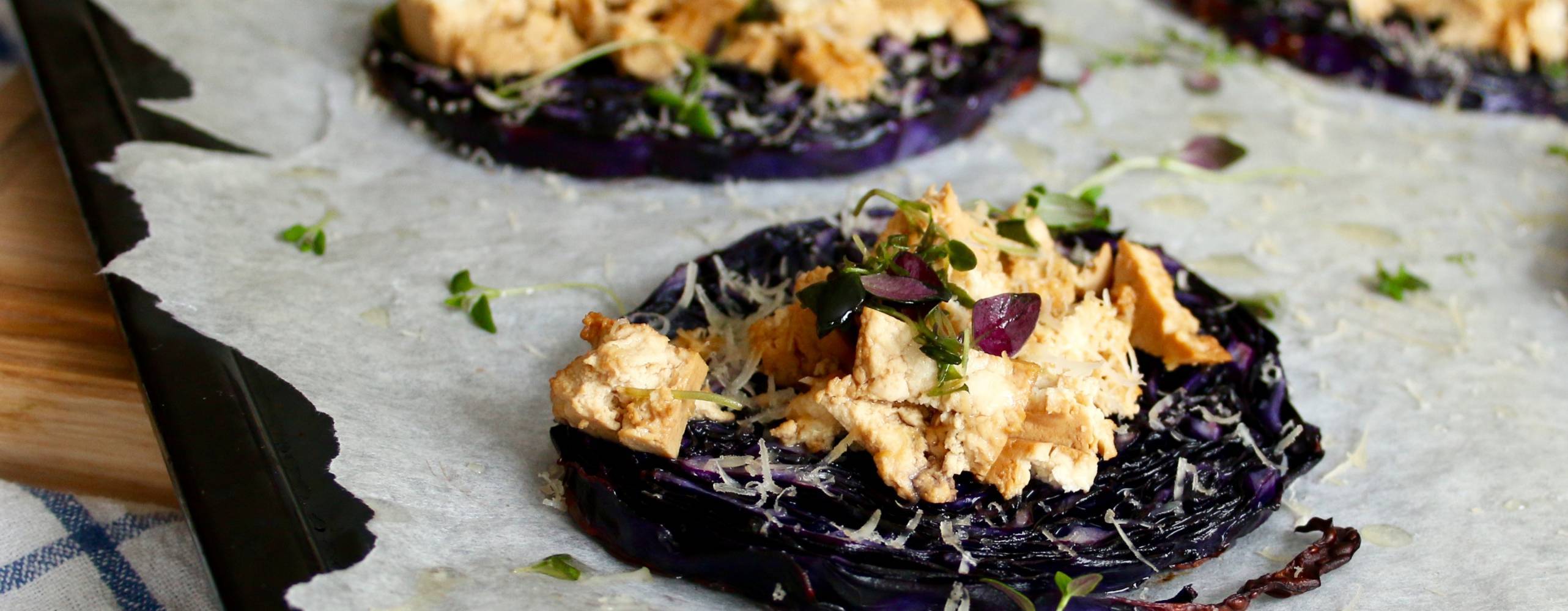 Rödkålskivor toppade med tofu och parmesan på ett bakplåtspapper.