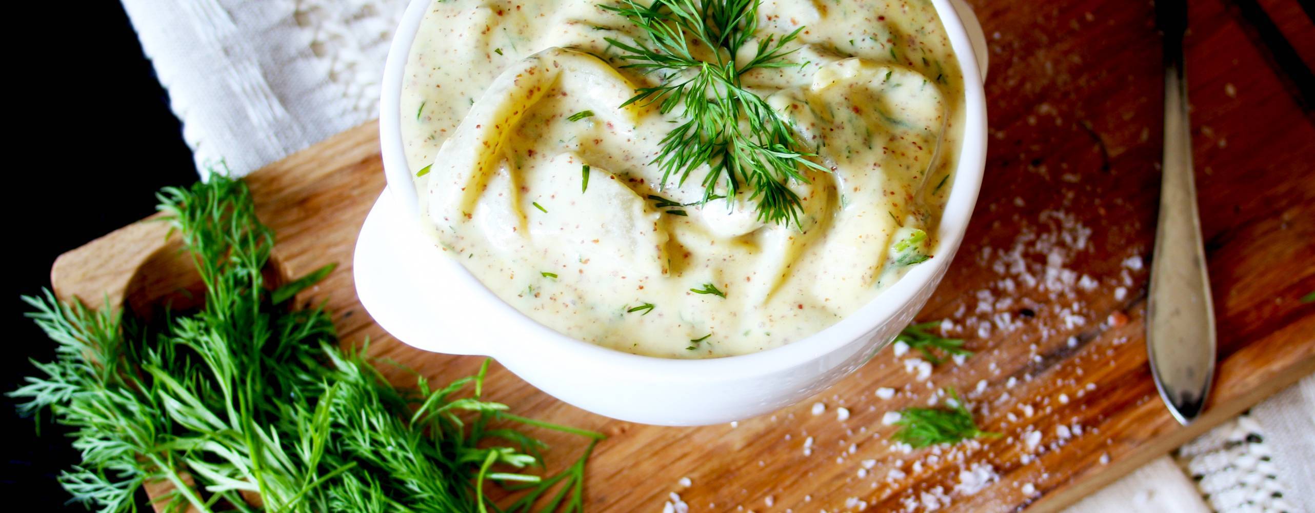 Auberginesill i senapssås i en skål på en skärbräda, garnerad med dill.