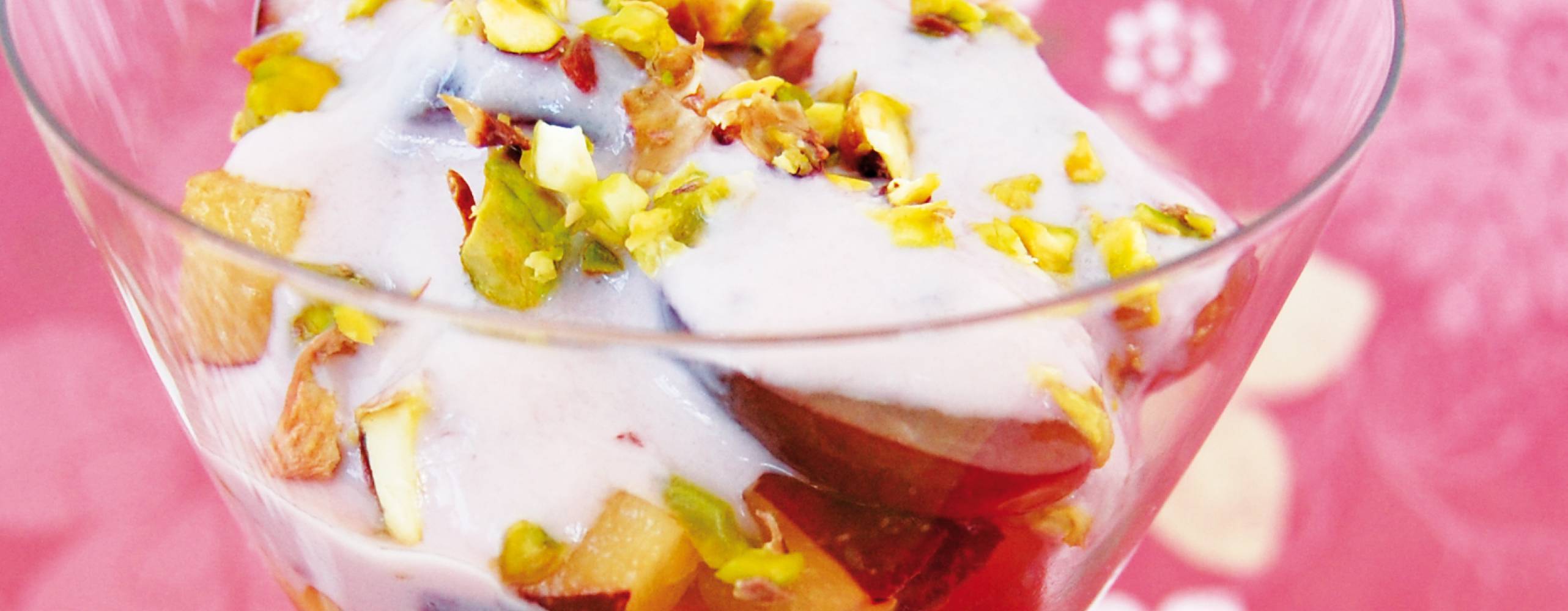 Fruktsallad med pistagenötter och vaniljyoghurt i en glasbägare.