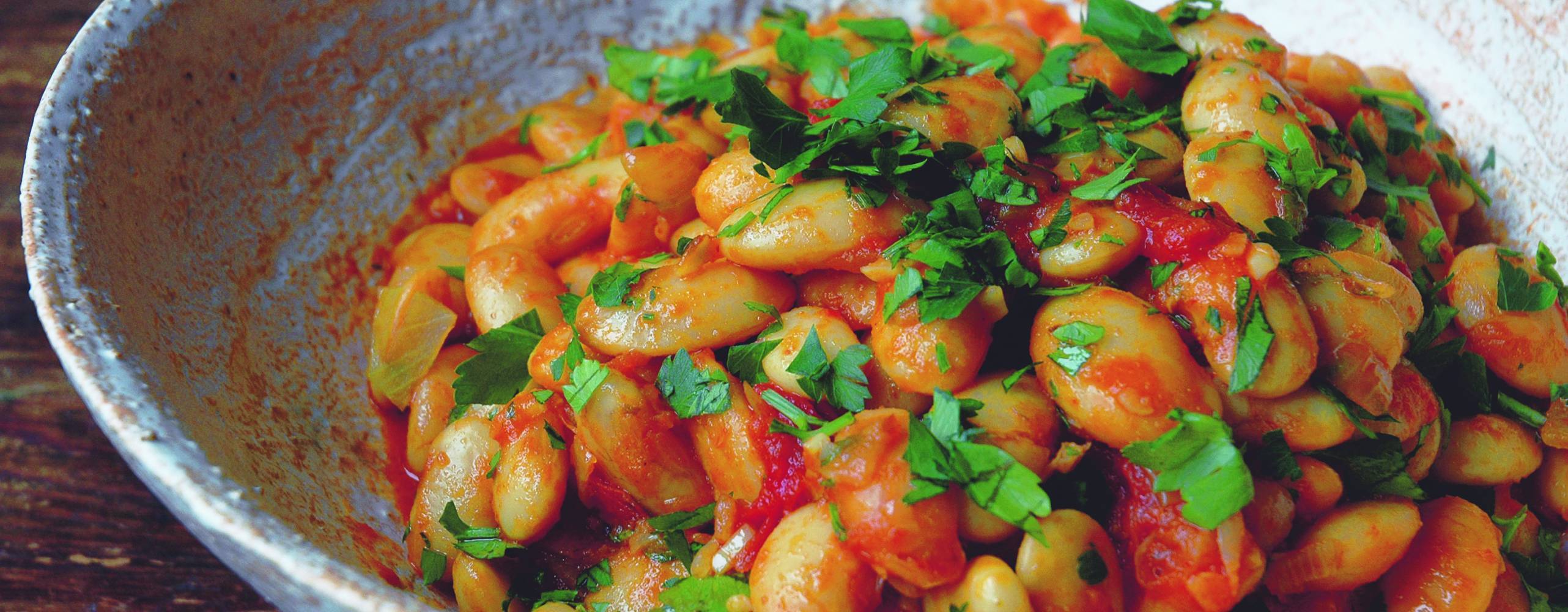 Ugnsbakade bönor i en skål, toppade med persilja.