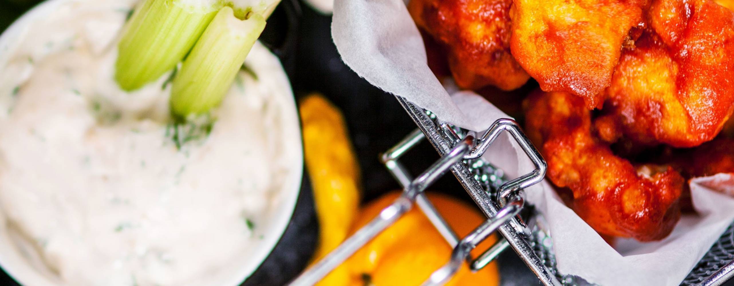 Buffalo wings av blomkål i en frityrkorg, bredvid står en skål med blåmögelostsås