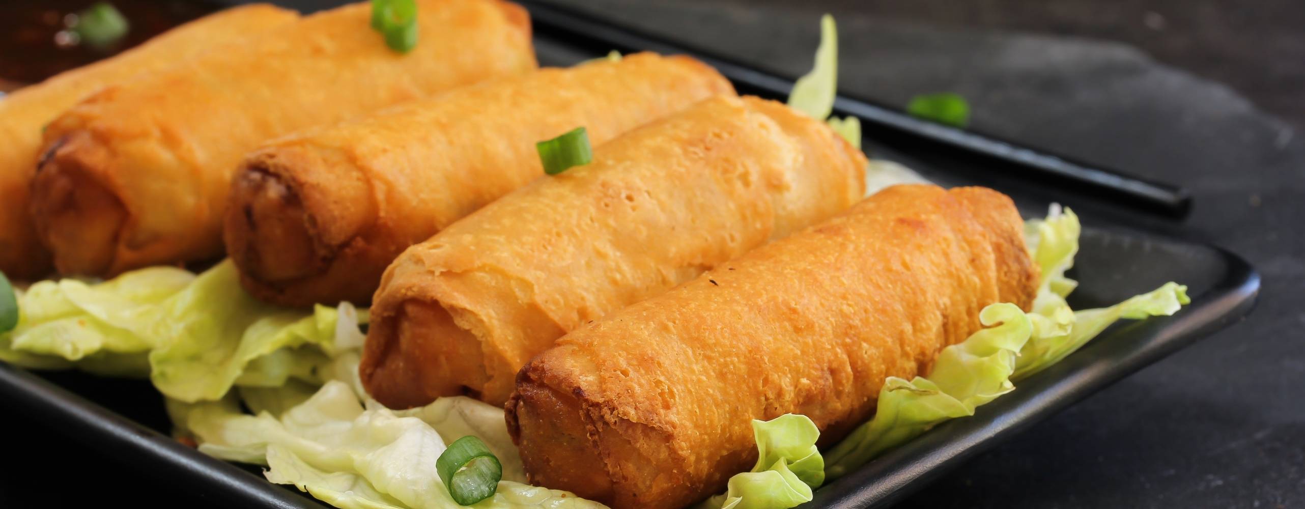 Fem vårrullar på en svart tallrik.