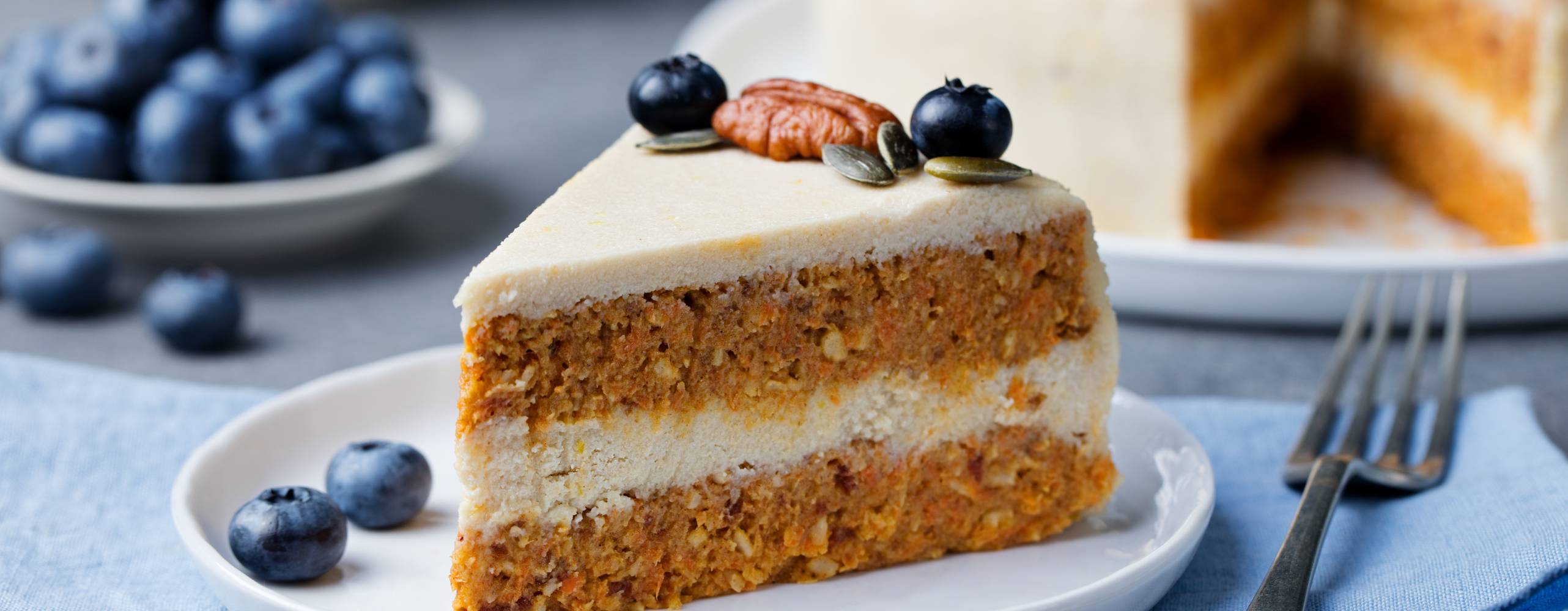 Vegansk morotskaka på en vit tallrik, bredvid tallrik ligger några blåbär