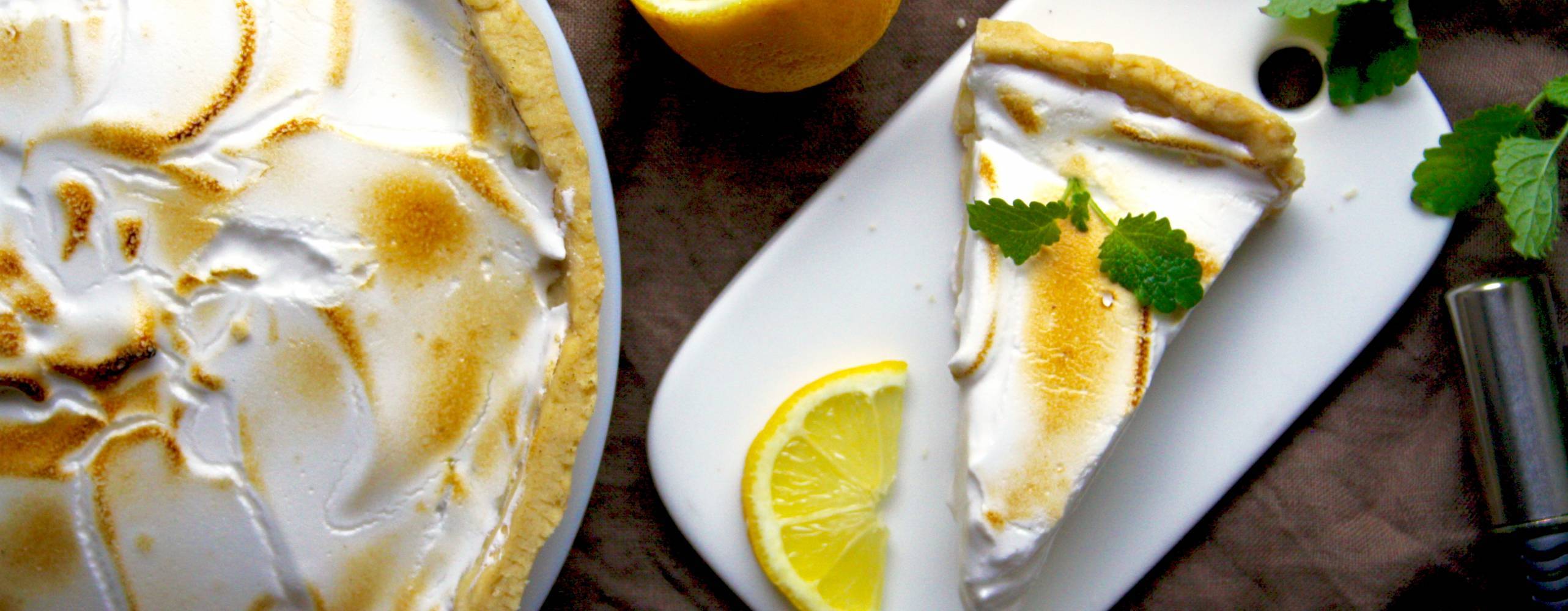 En citronpaj med marängtäcke, bredvid pajen ligger några delade citroner