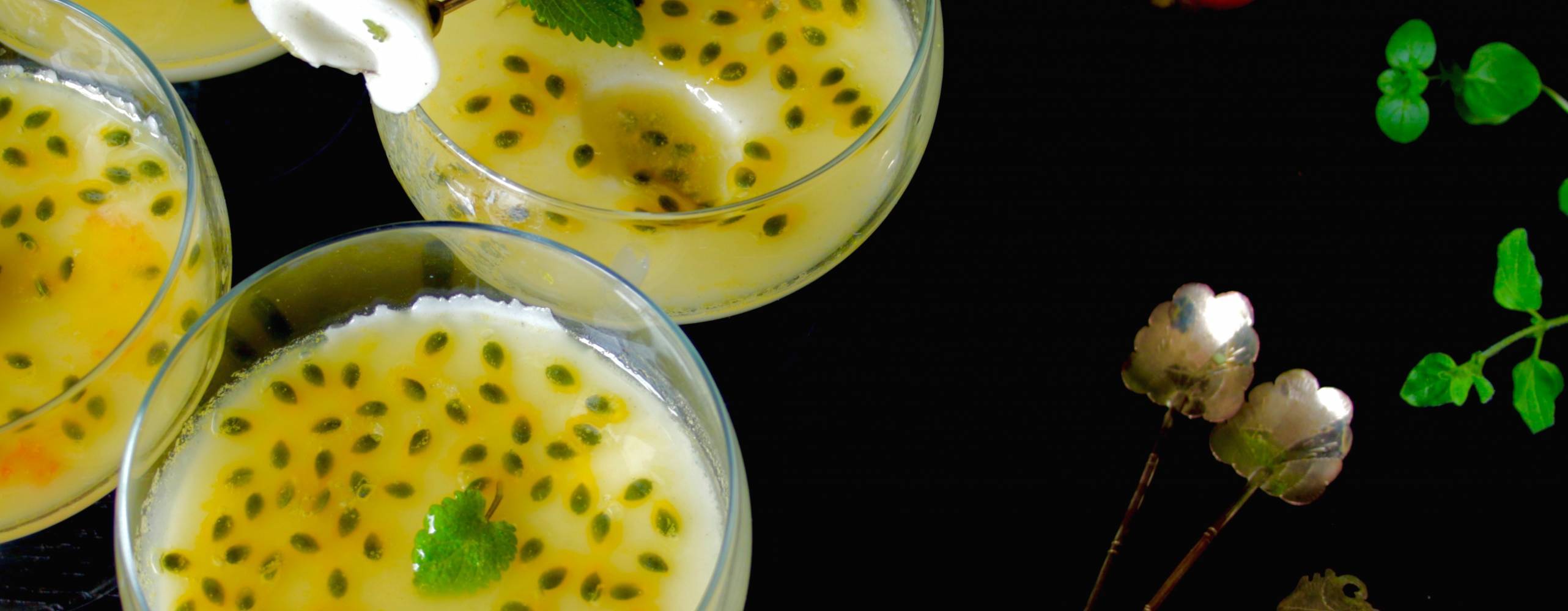 Fyra bägare med pannacotta med passionsfrukt på ett mörkt bord.