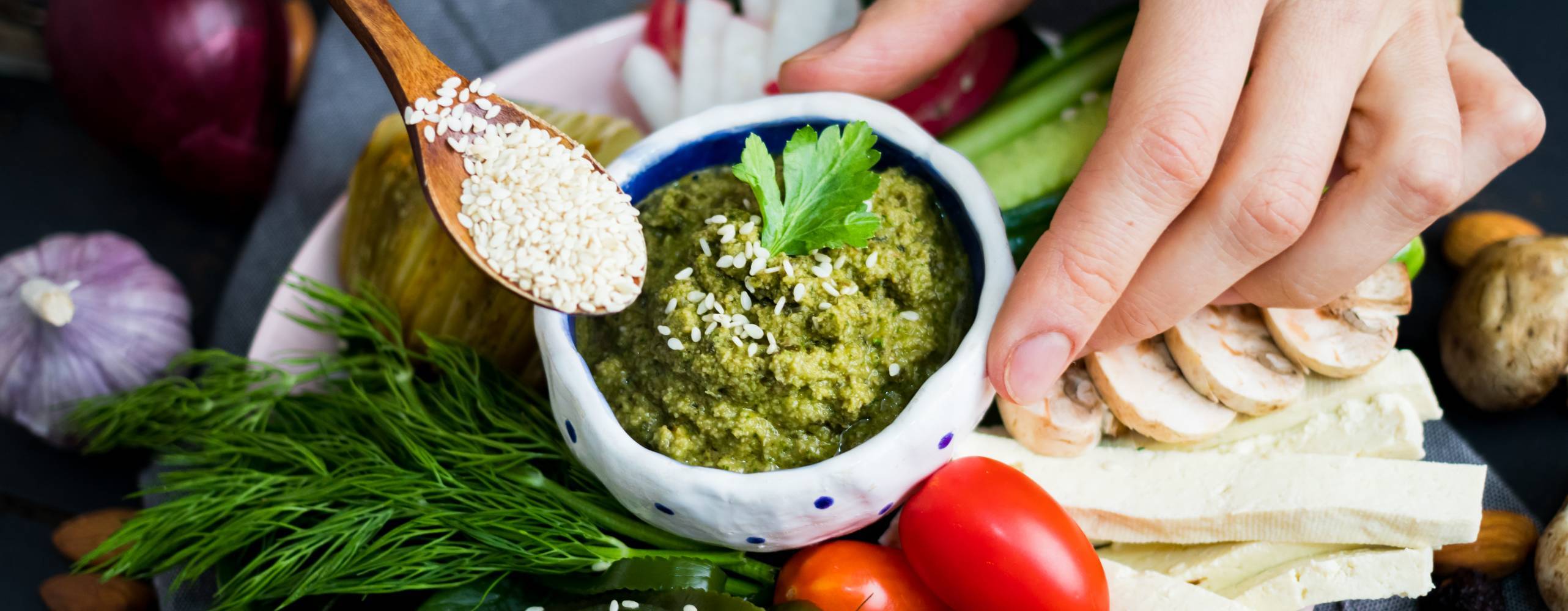 Woman hand adds sesame seeds to healthy veggie buddha bowl with vegetables - cucumbers, tomatoes, radish, mushrooms, seaweed, garlic, avocado chickpea dip. Closeup view. Raw, vegan, vegetarian food Av Viktor Kochetkov Thumbnail