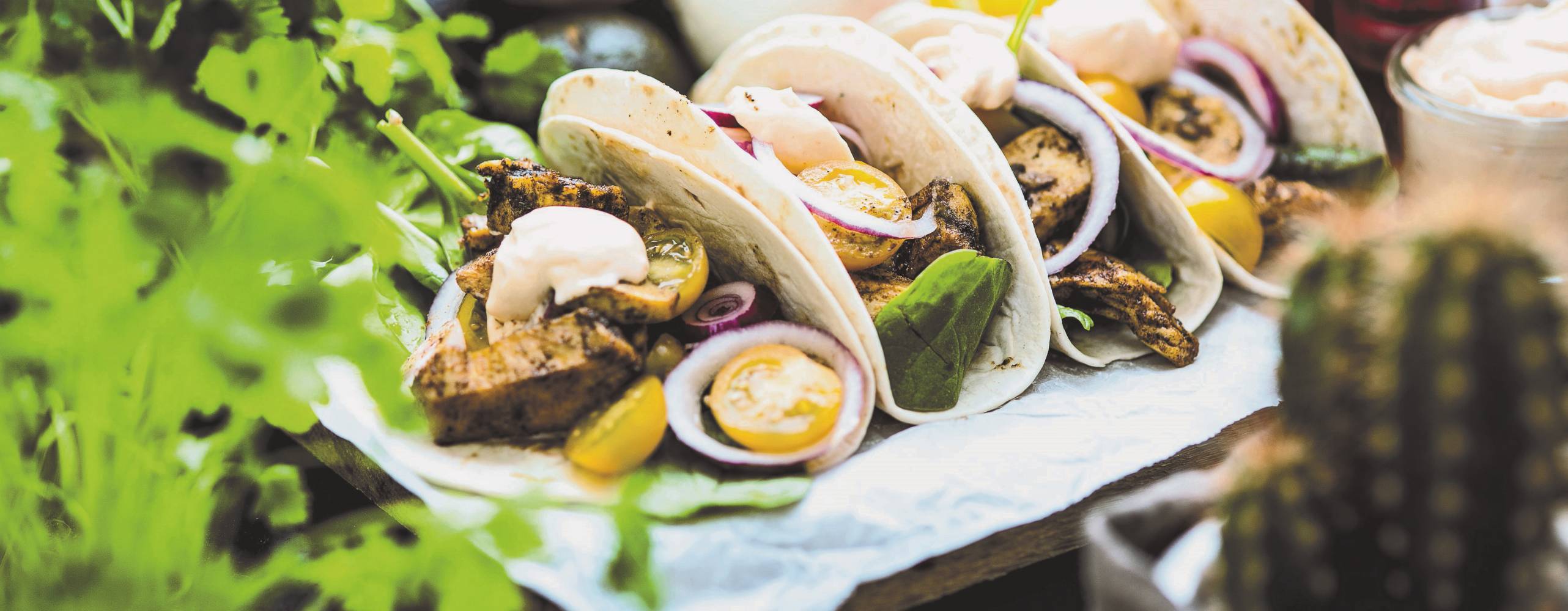 Fyra stycken tacos ligger på en vit handduk, i förgrunden syns gröna blad