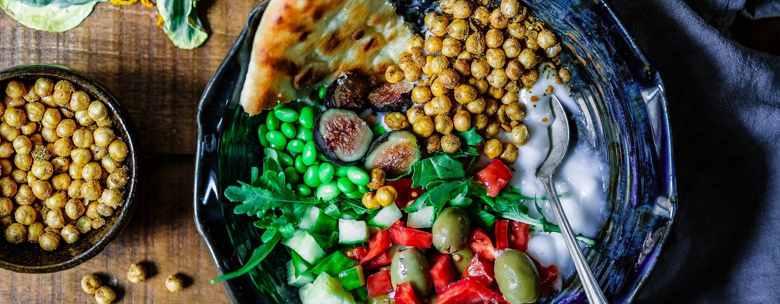 skål med kikärtor, grönsaker och sås på ett bord