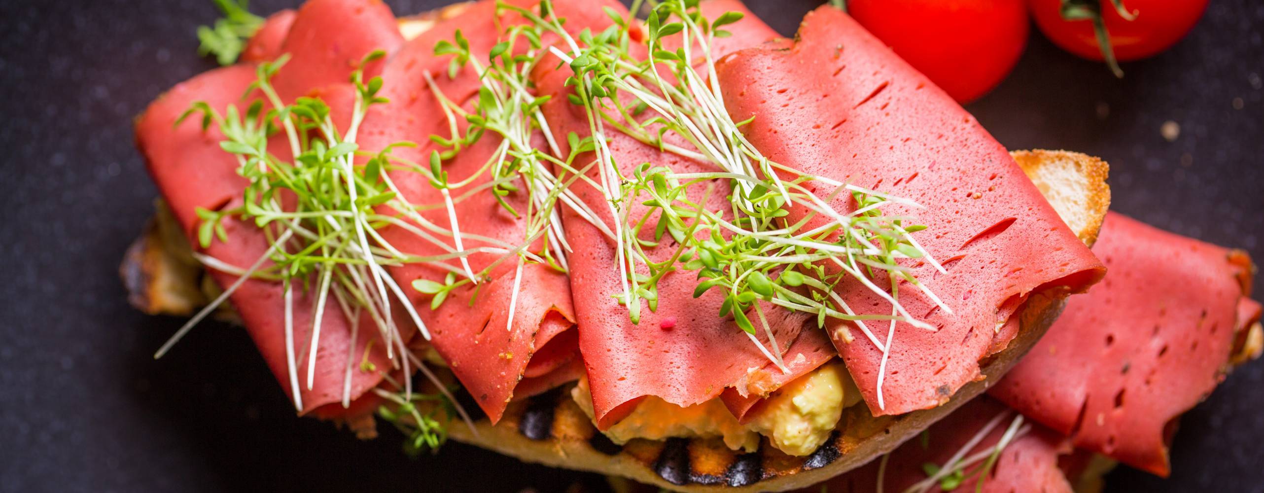 Vegansk skinka på en macka toppad med en gröna blad