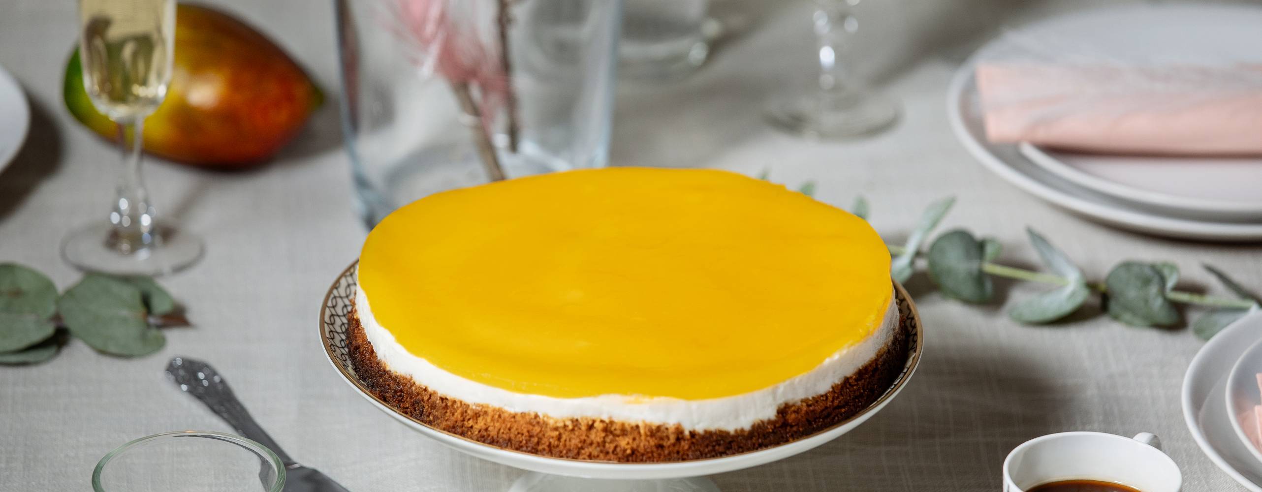 Vegansk cheesecake med mangoglasyr på ett tårtfat.