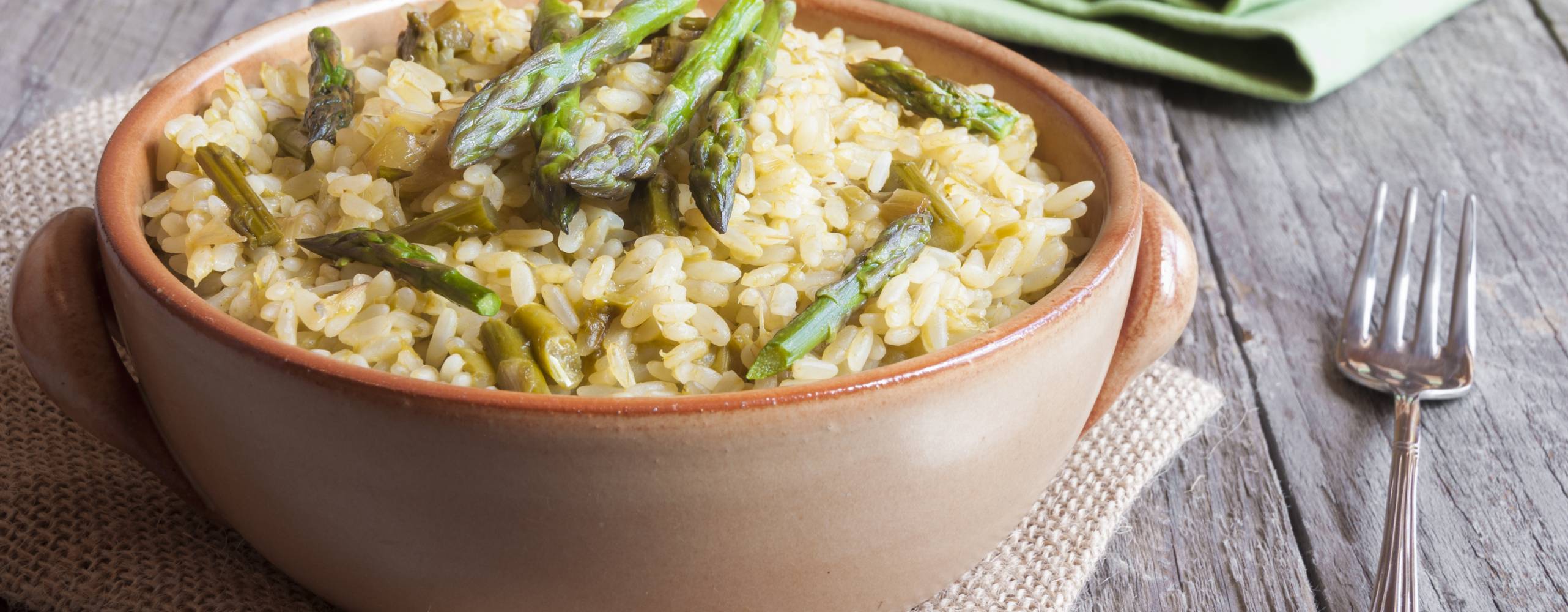 Skål med risotto toppad med sparris på ett bord