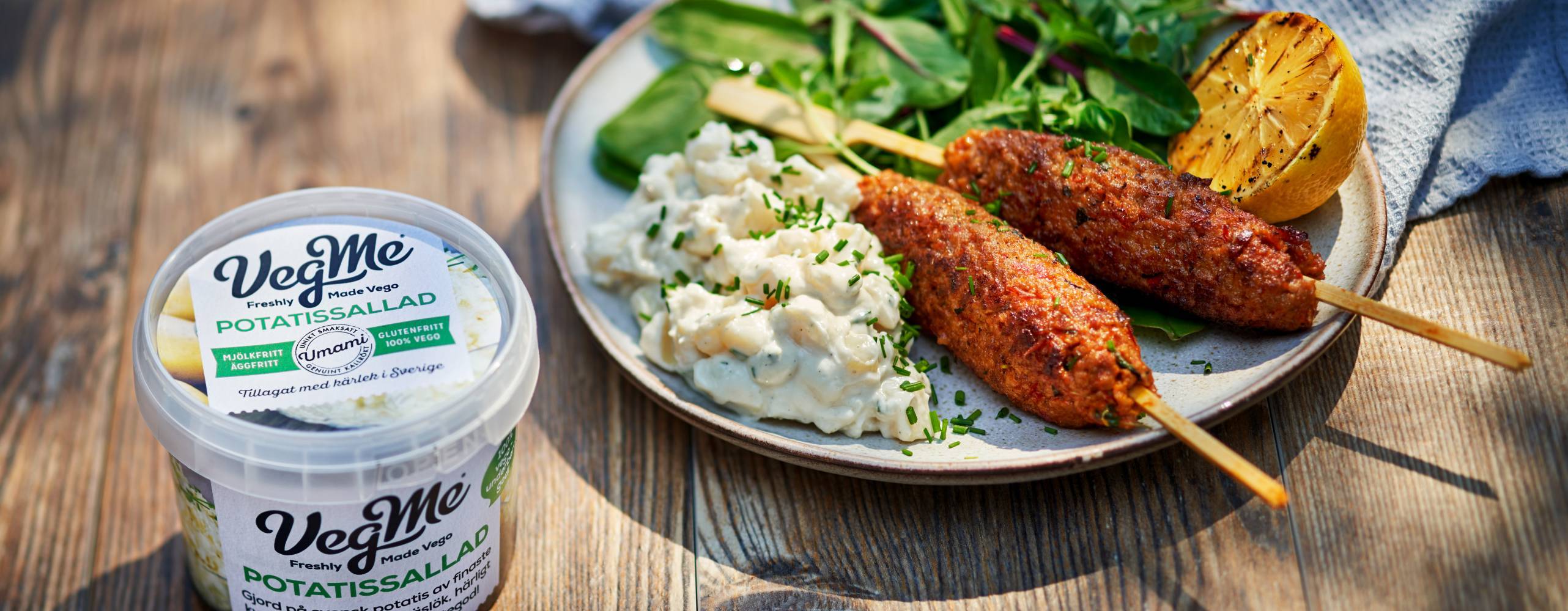 Förpackning av potatissallad intill en tallrik med potatissallad med vegansk spett