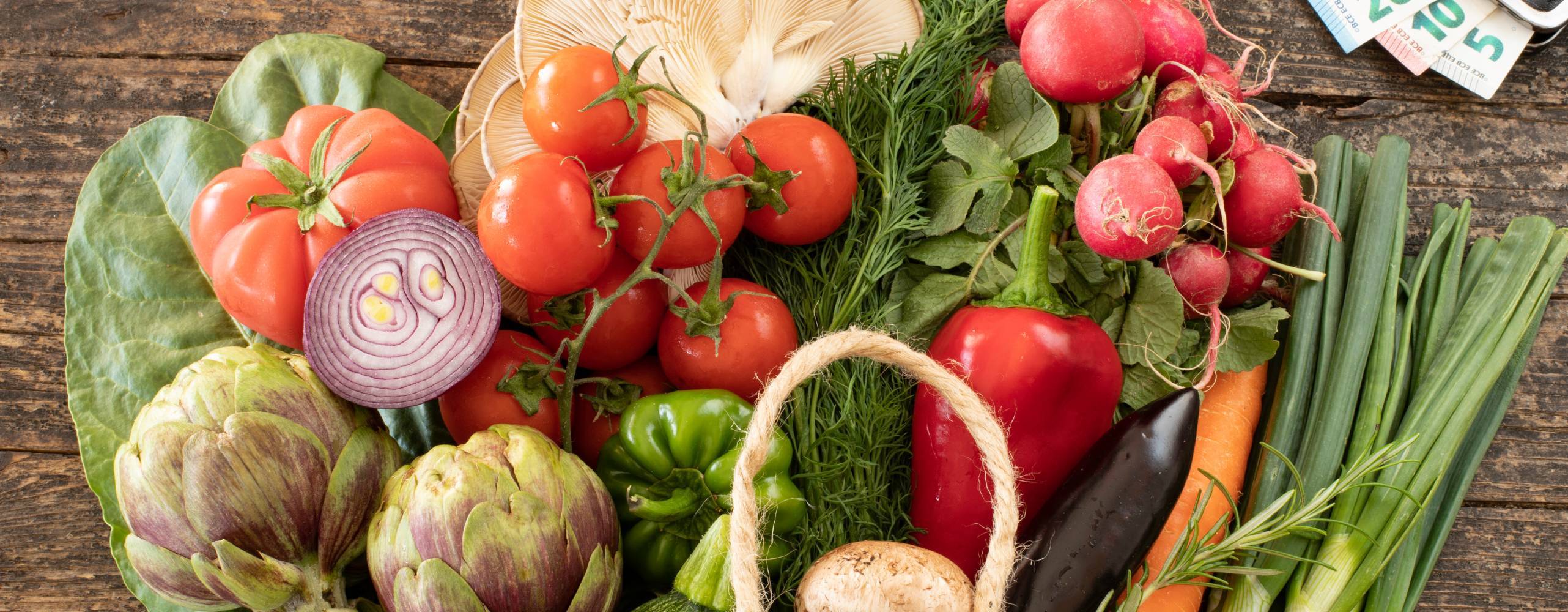 Grönsaker i en korg intill en plånbok med sedlar