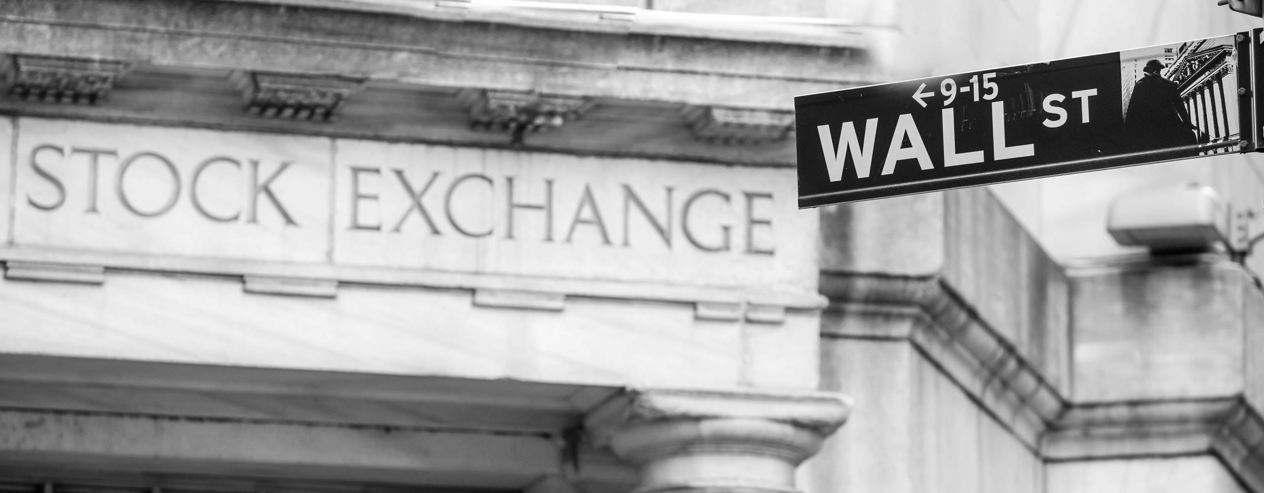 Bild på vägskylt med texten "wall st" framför en mur med texten "Stock exchange"