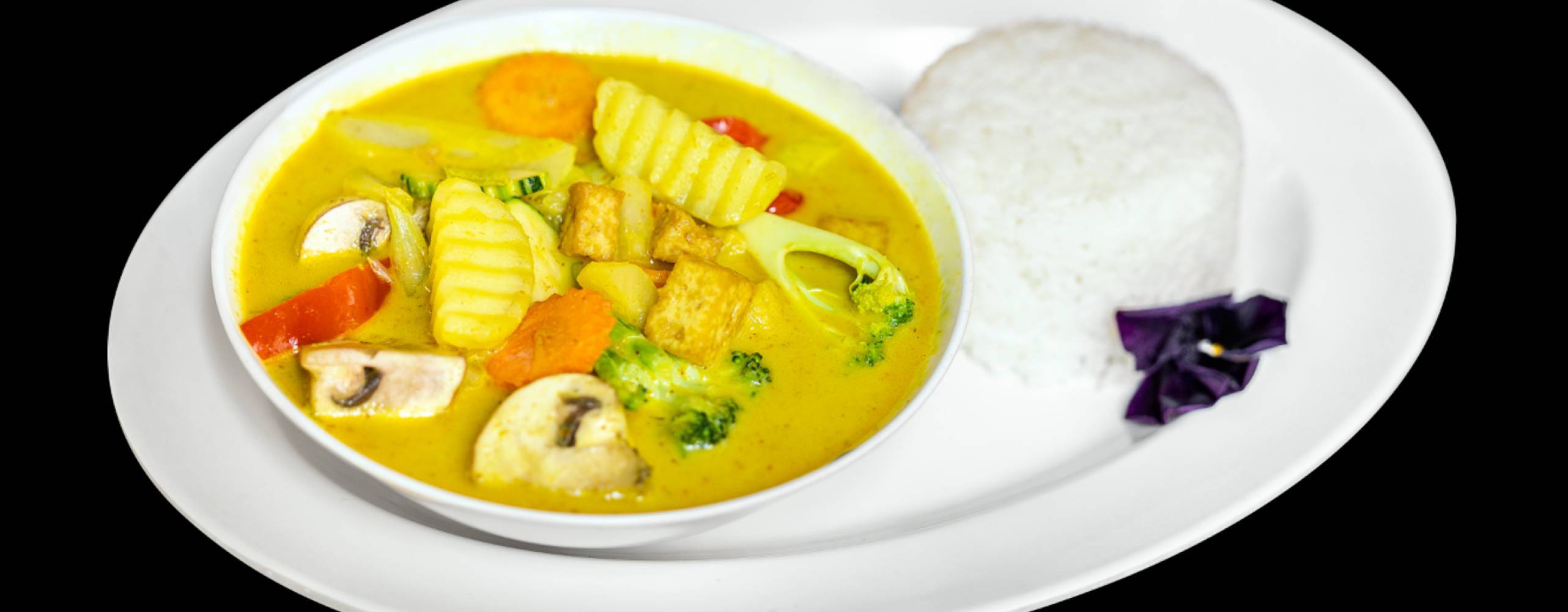 Mae Thai Stockholms veganska gula curry med tofu, grönsaker och ris på en vit tallrik med svart bakgrund.