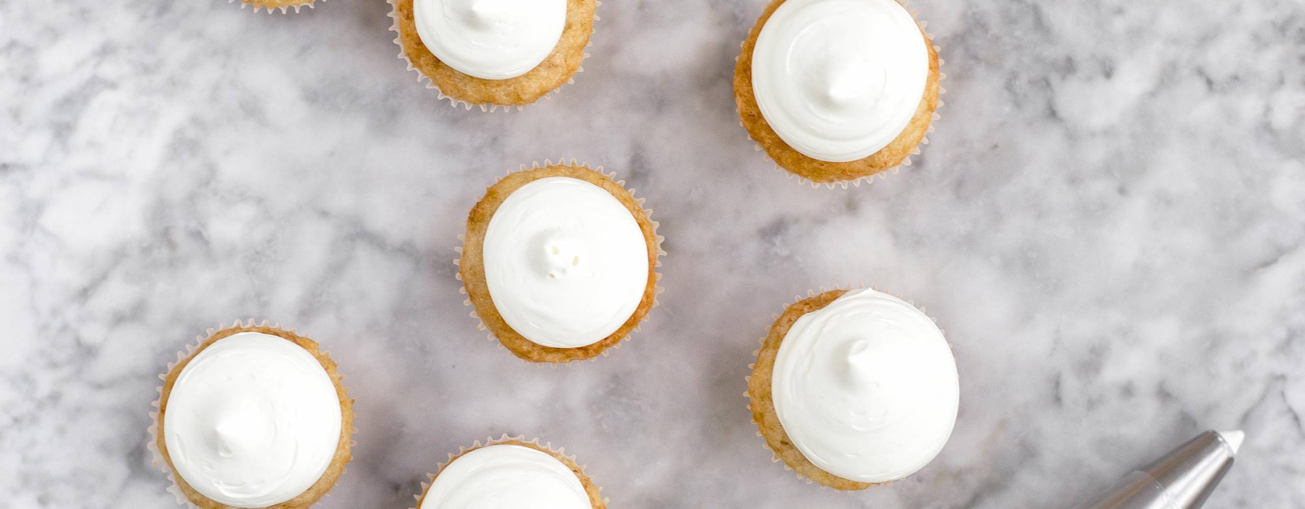 Bananmuffins med aquafaba har här gräddats i minimuffinsformar i 175°C i 13-15 minuter. Godisfluff av smälta bananskumgodisar är spritsat med en rund spritstyll på en centimeter.