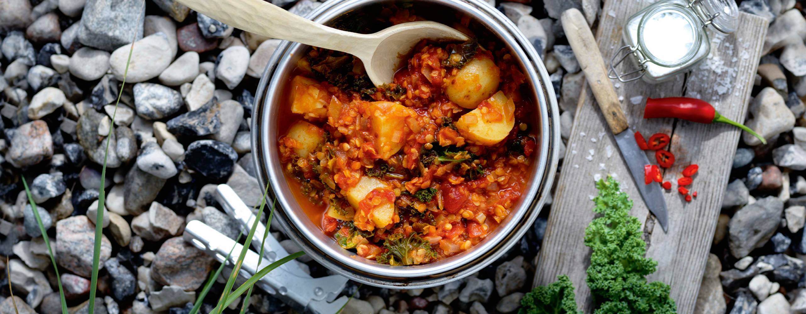Potatis one pot i en gryta på småstenar med en träbräda med en kniv, röd chili och flingsalt bredvid