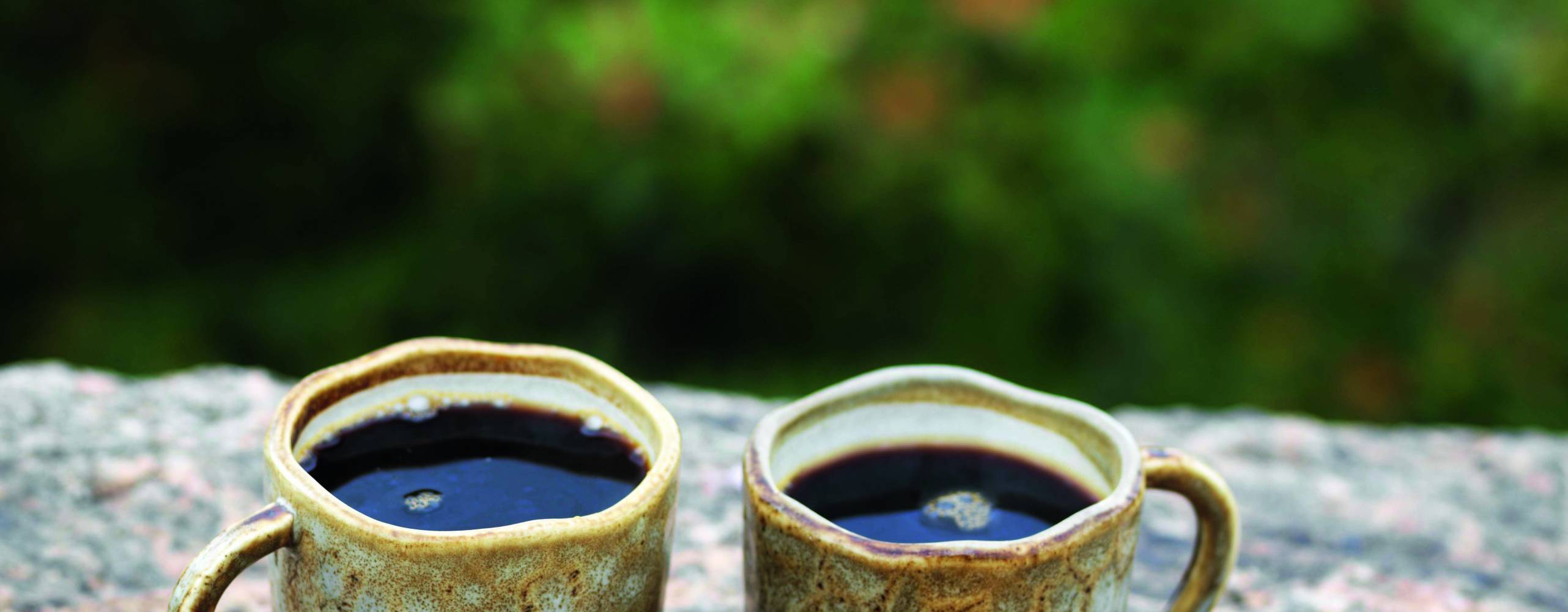 två tahinicookies på en sten med två kaffekoppar bakom
