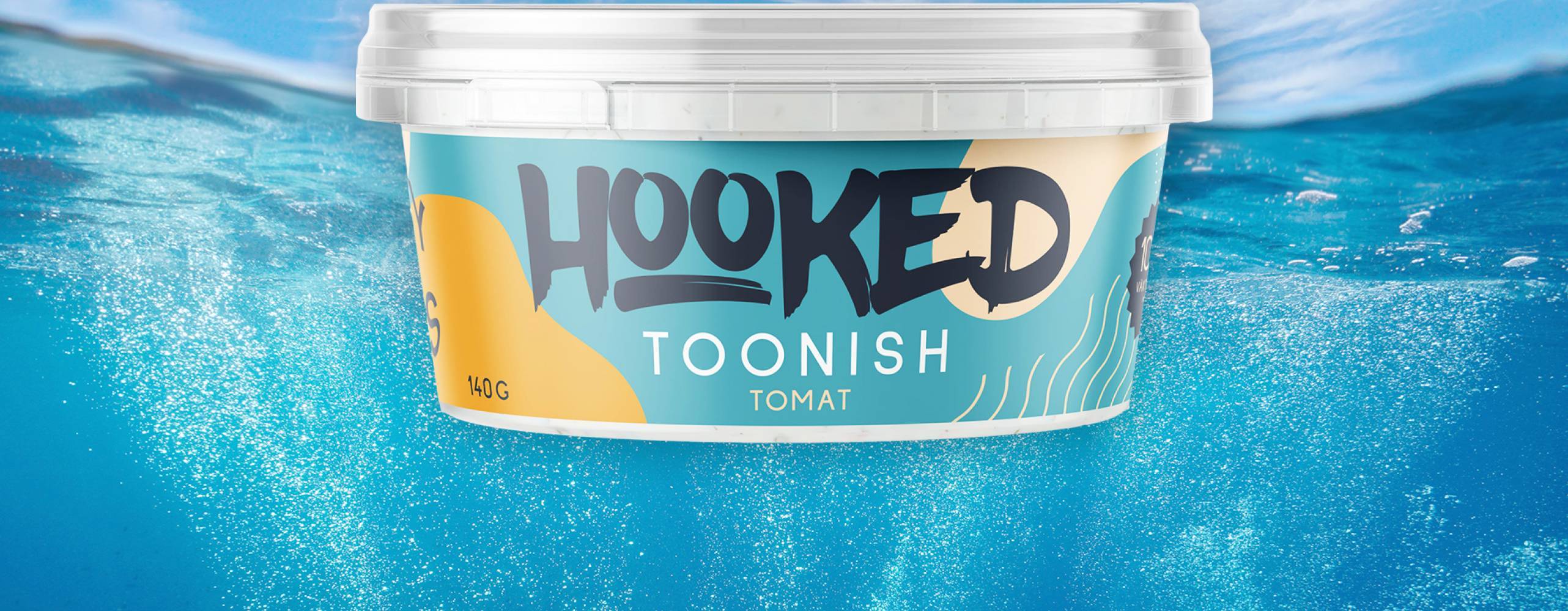 Plastburk med "Toonish" i smaken tomat mot bakgrundsfoto föreställande himmel och hab, taget delvis under vattenytan.