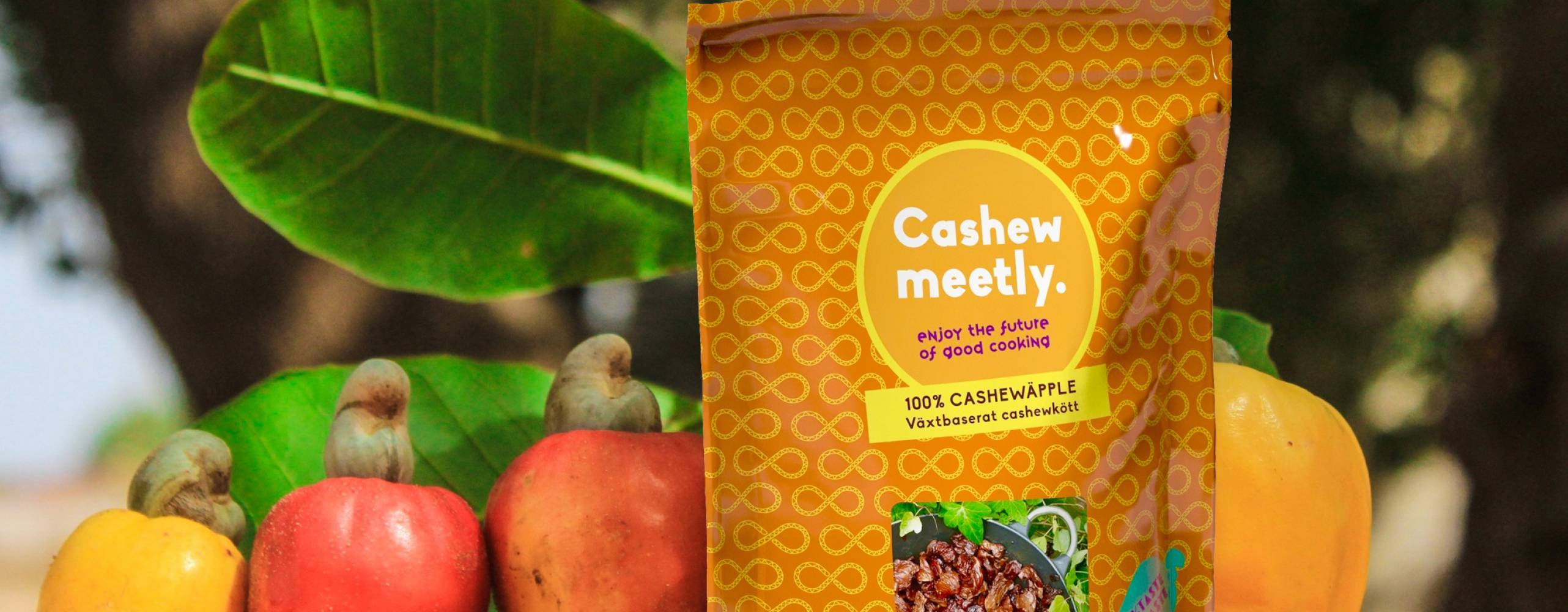 Cashewmeetly i förpackning med cashewäpplen och grönska i bakgrunden.