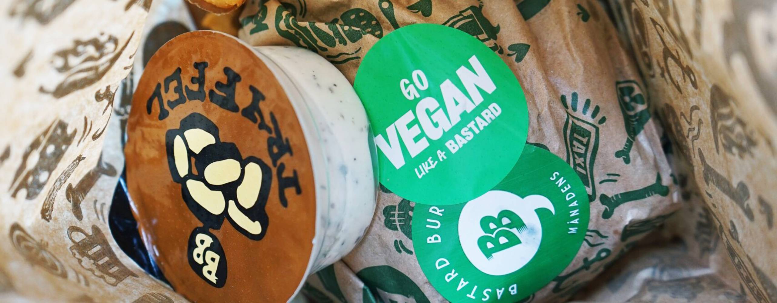 Burgare, pommes och sås från Bastard Burgers i papperspåse. På burgaren finns ett klistermärke med texten "Go vegan like a bastard".