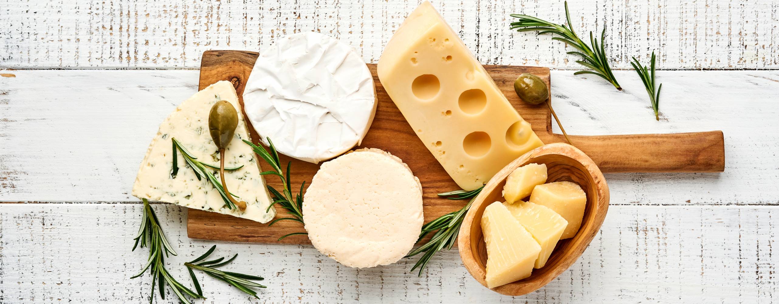 Flera olika mejeriostar på en träbricka på ett vitt bord.