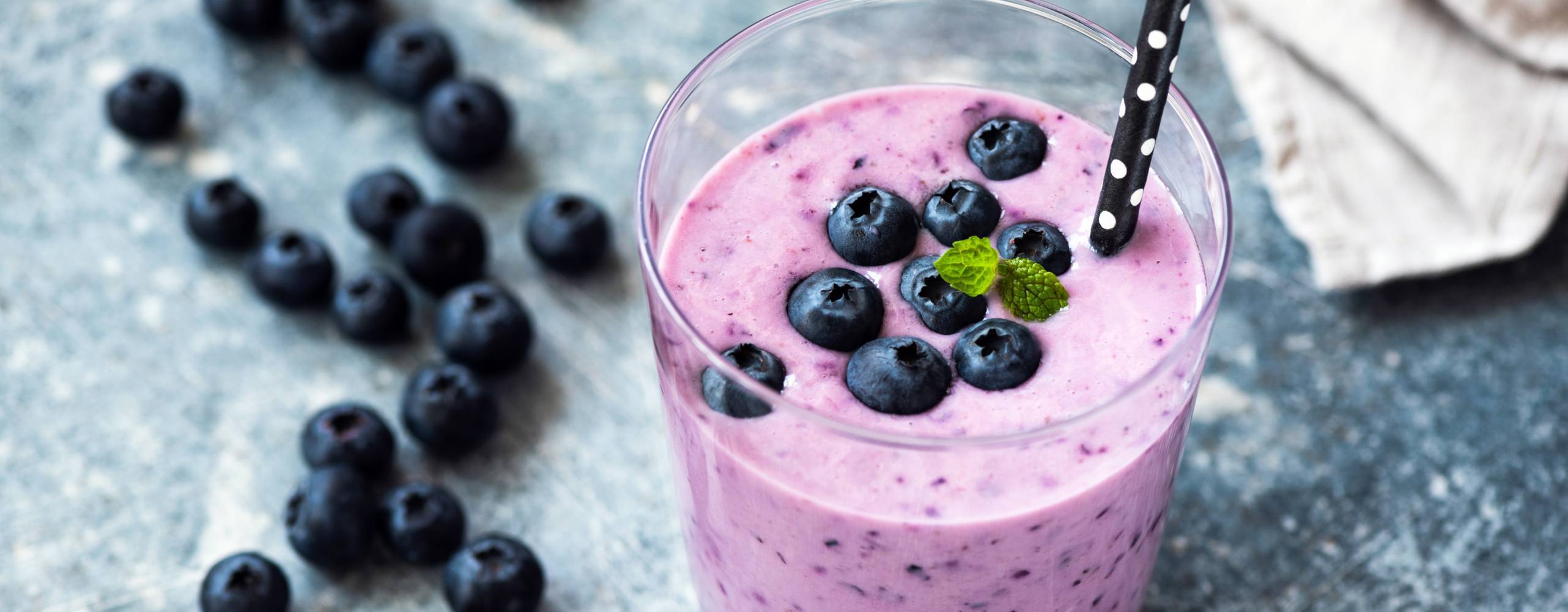 Blåbärssmoothie i ett glas med sugrör i papp med blåbär som garnering.