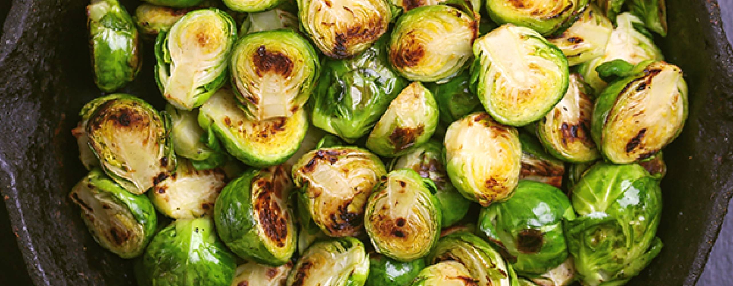 stekt brysselkål i en svart serveringsskål på ett mörkt bord