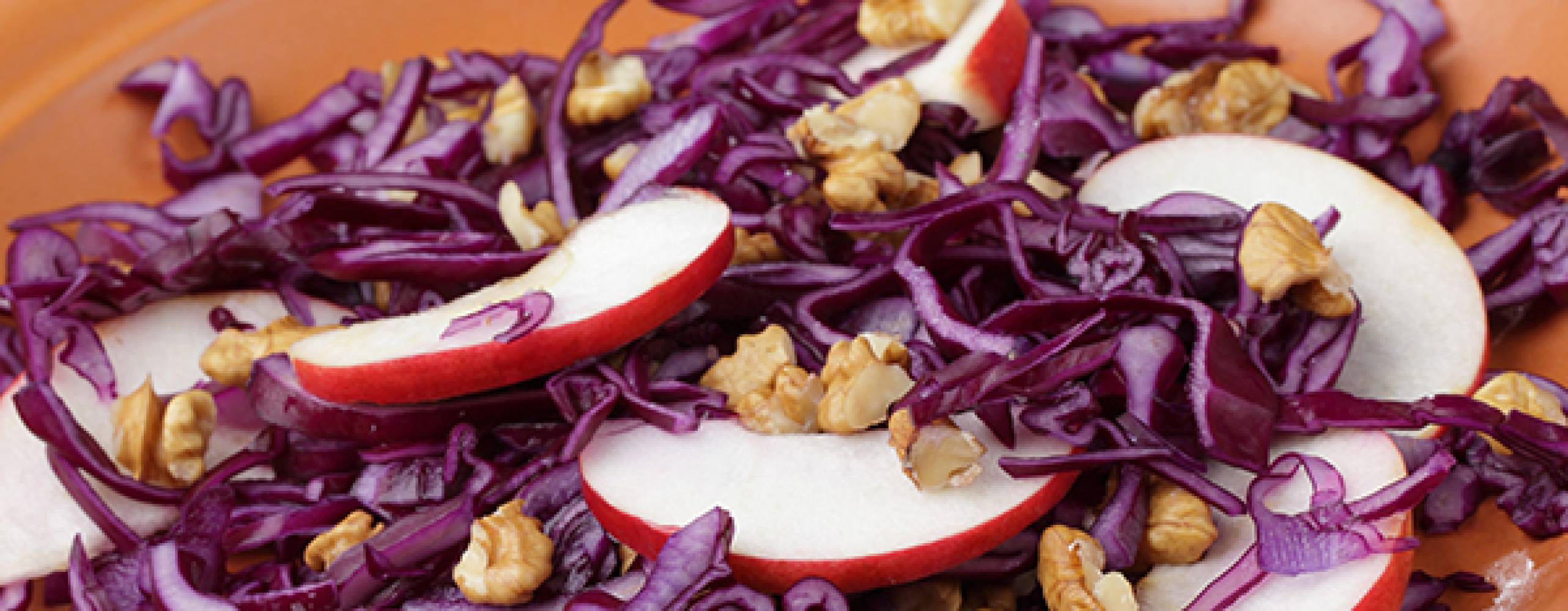 Rödkålssallad med äppelskivor och valnötter i ett keramikfat.