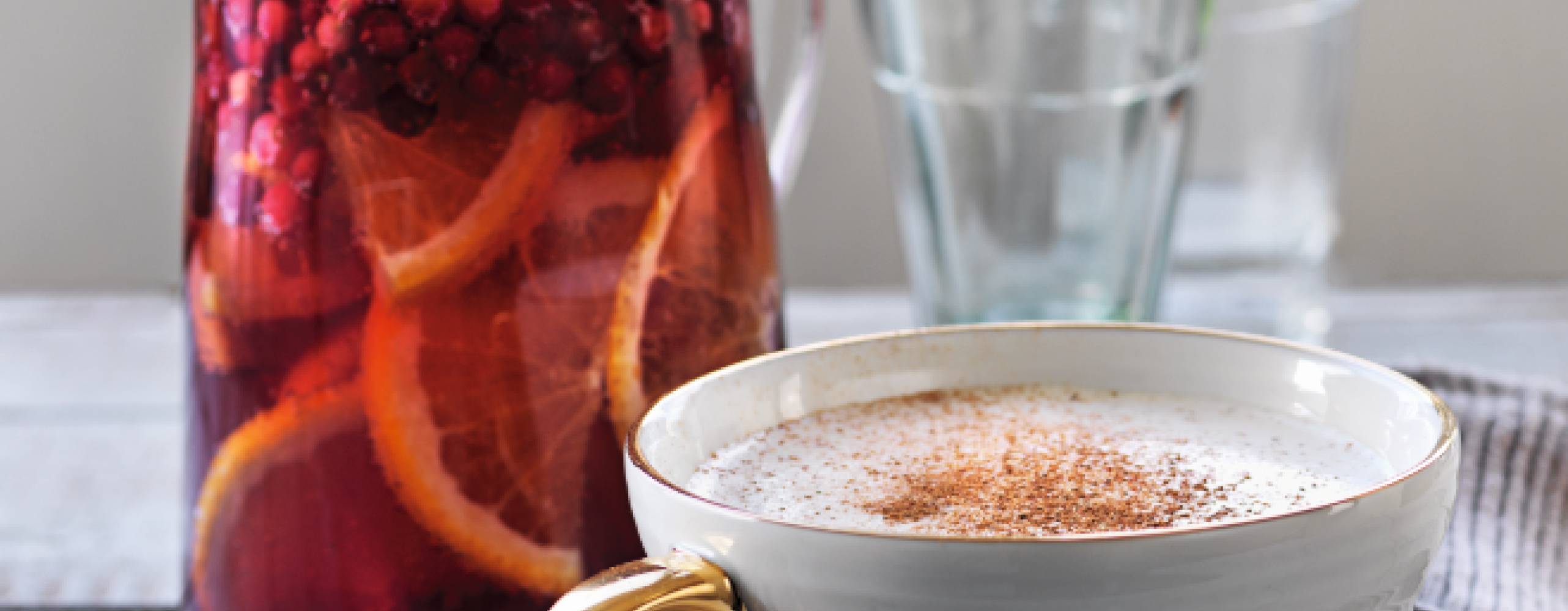 Toddy i en vit mugg med guldhandtag bredvid en karaff med sangria.
