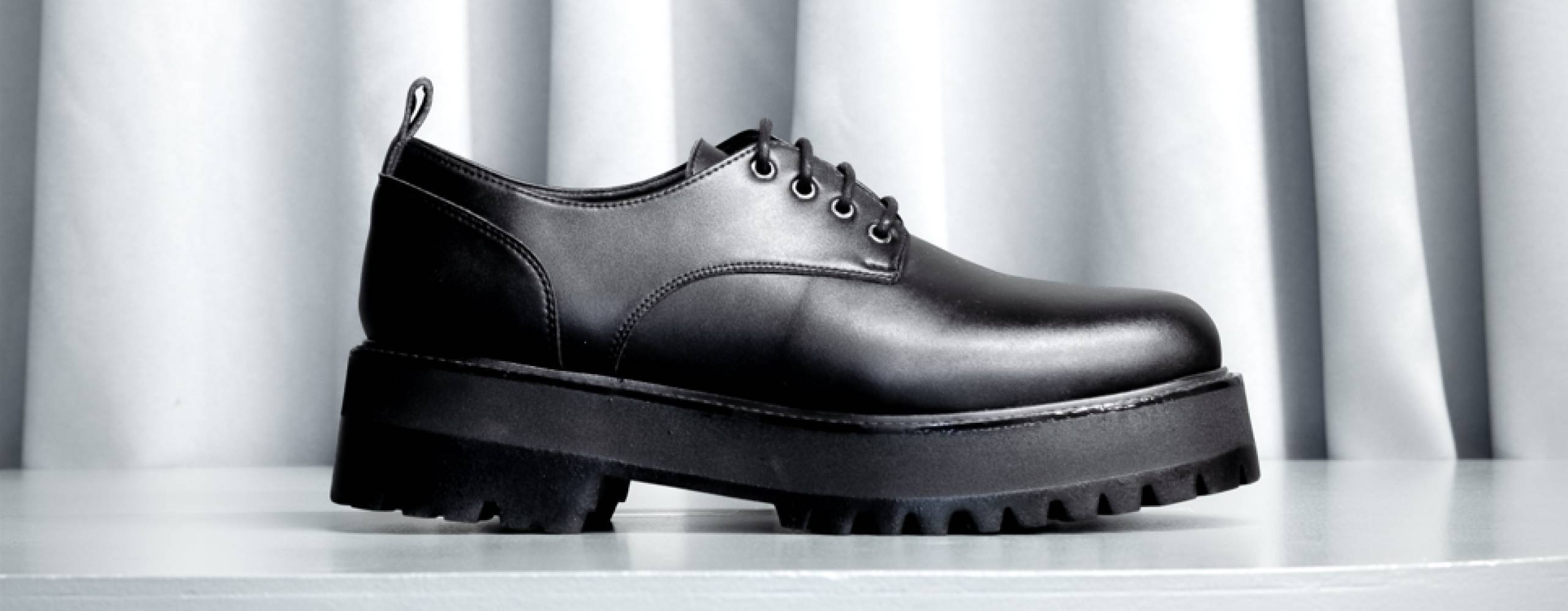 Svart veganska låg känga mot ett ljusgrått draperi