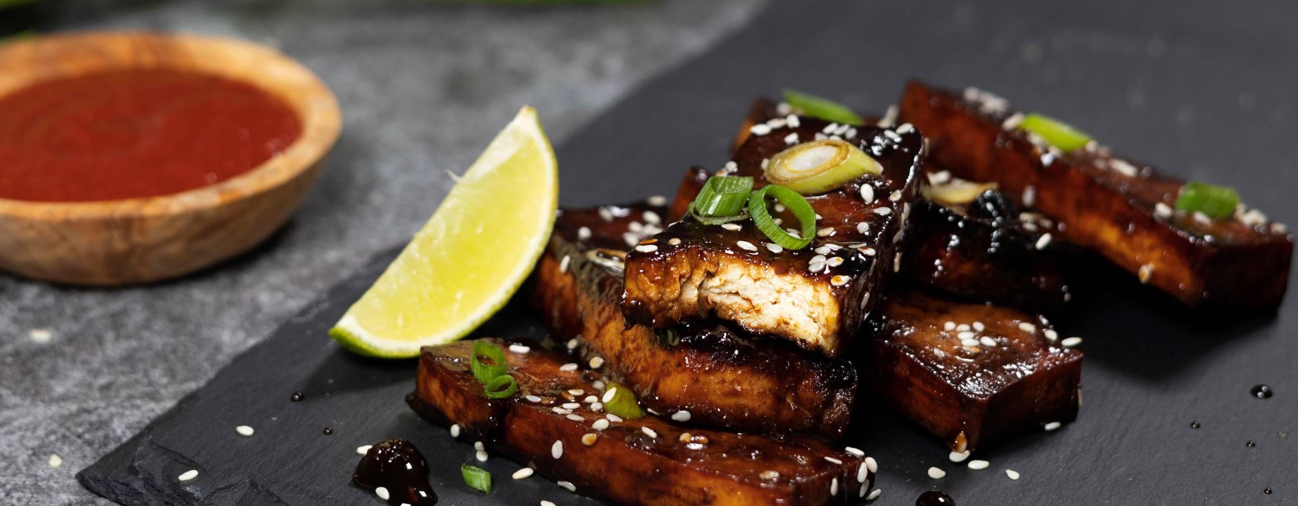 Veganska revbensspjäll av tofu som ligger på ett svart stenblock mot en grå bakgrund