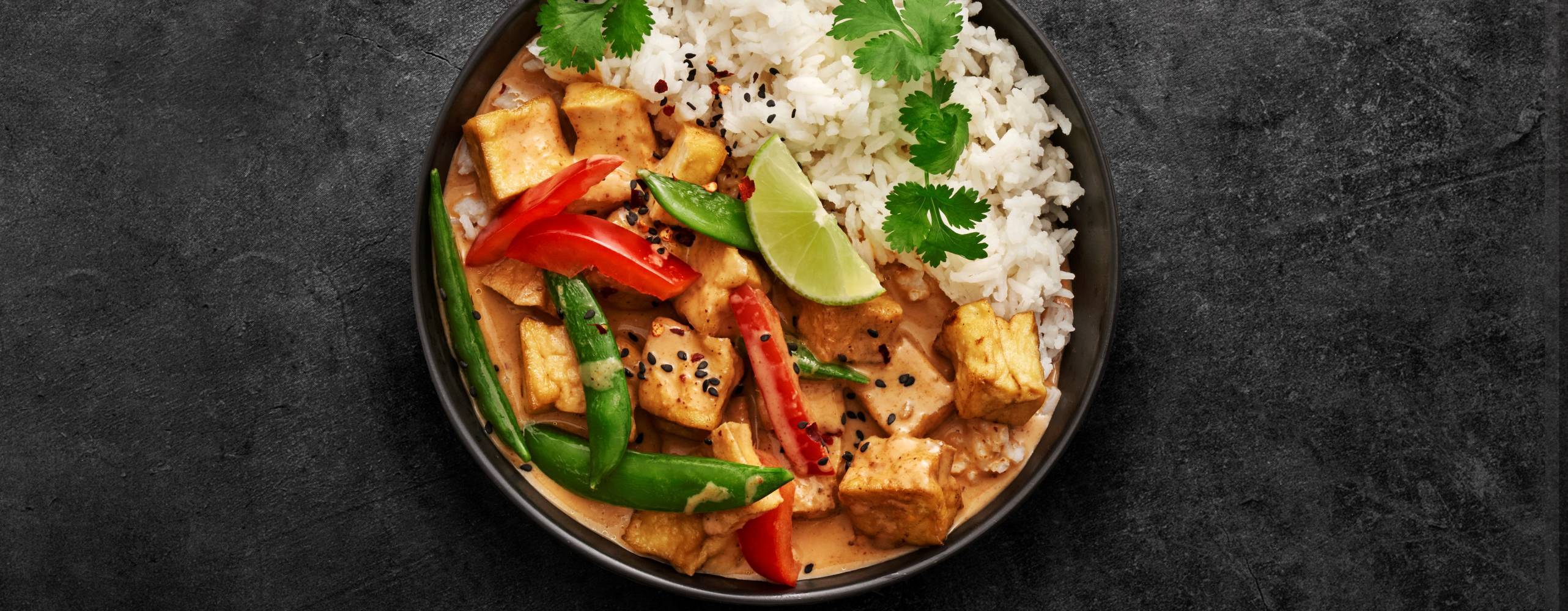 röd currygryta med ris i en djuptallrik vinkel uppifrån mot en granitgrå bakgrund