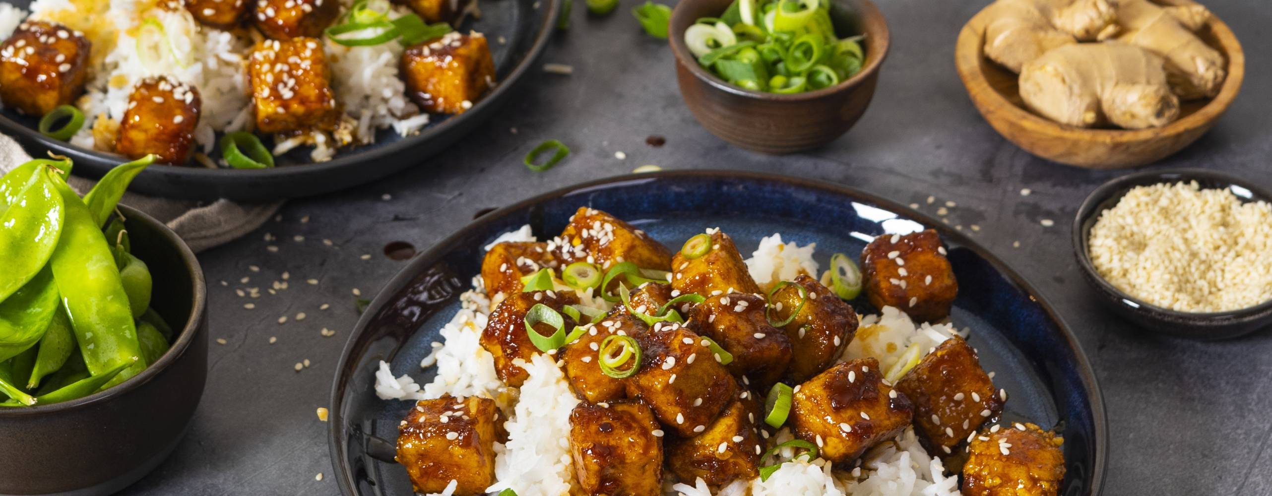 Två djuptallrikar med general tso tofu på ett mörkgrått bord