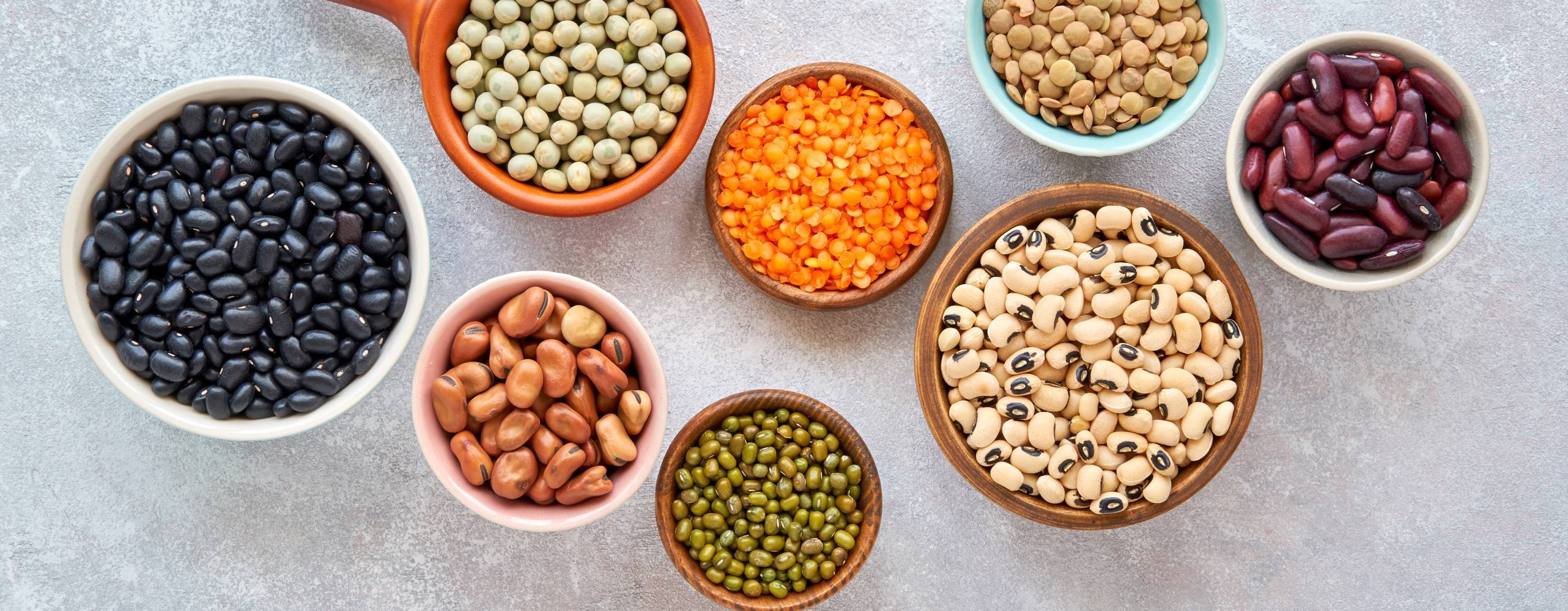 Baljväxter och bönor sortiment i olika skålar på ljus sten bakgrund. Toppvy. Hälsosam vegansk proteinmat.