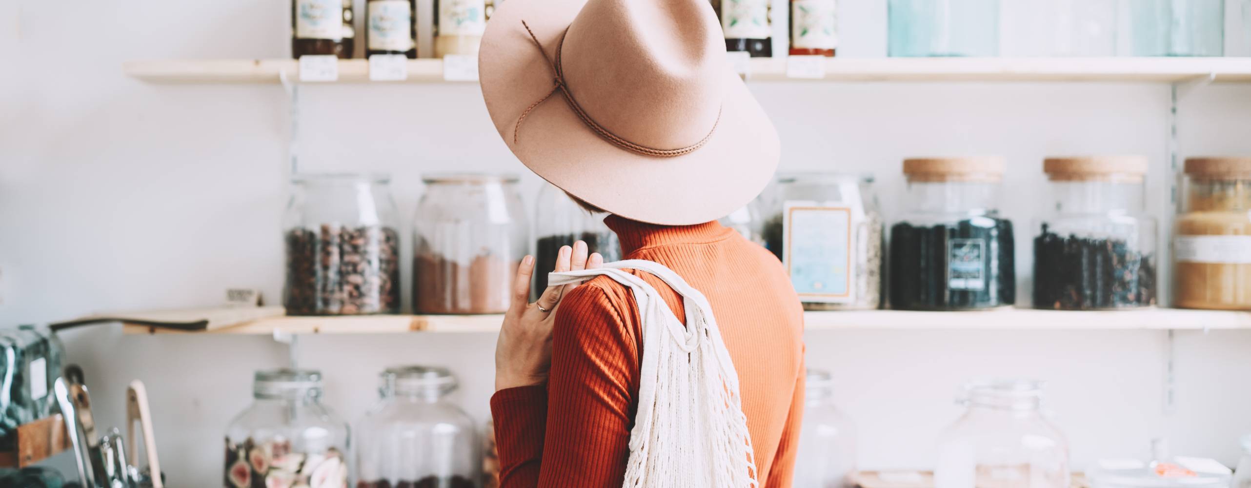 Minimalistisk vegansk stil ung kvinna med bomull återanvändbara nät väska på bakgrund av varor av noll avfallsbutik. Shopping utan plastförpackning i plastfri livsmedelsbutik.