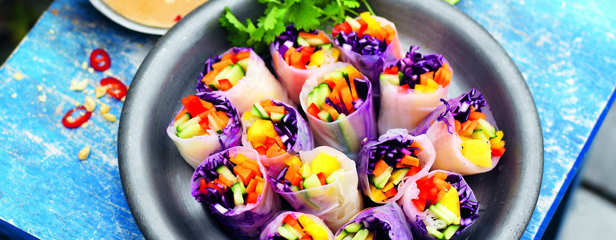 Vietnamesiska vårrullar i ett fat på ett turkost bord ute i naturen